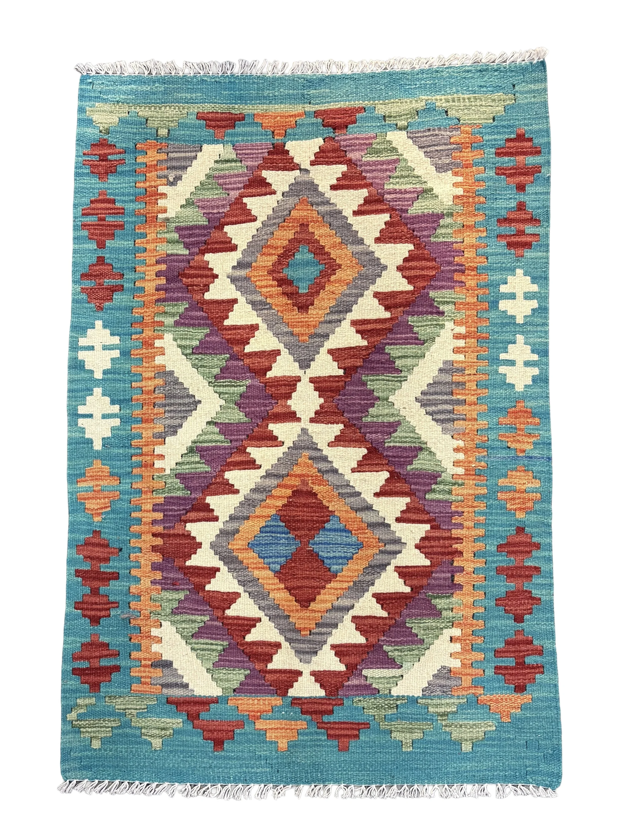 Colorful geometric patterned rug with fringe on top and bottom, featuring a diamond shape in the center with surrounding angular designs in shades of red, purple, orange, green, cream, and blue.
