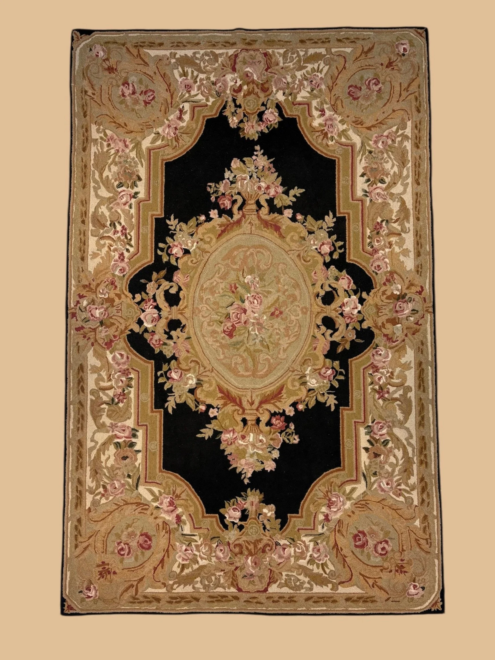 A decorative area rug with a black background, floral motifs in pink and beige, and a central medallion in cream and pink shades.