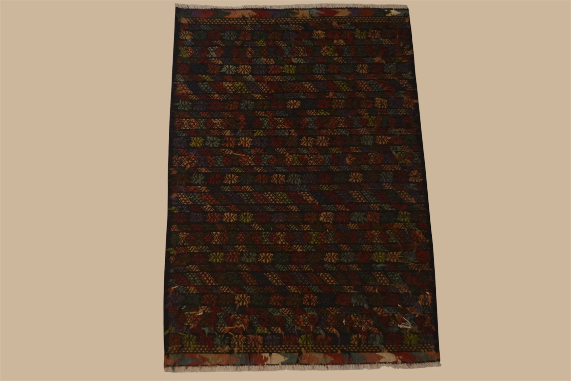 A woven rug with intricate geometric and floral patterns in dark colors like black, red, and green, laid out on a beige floor.