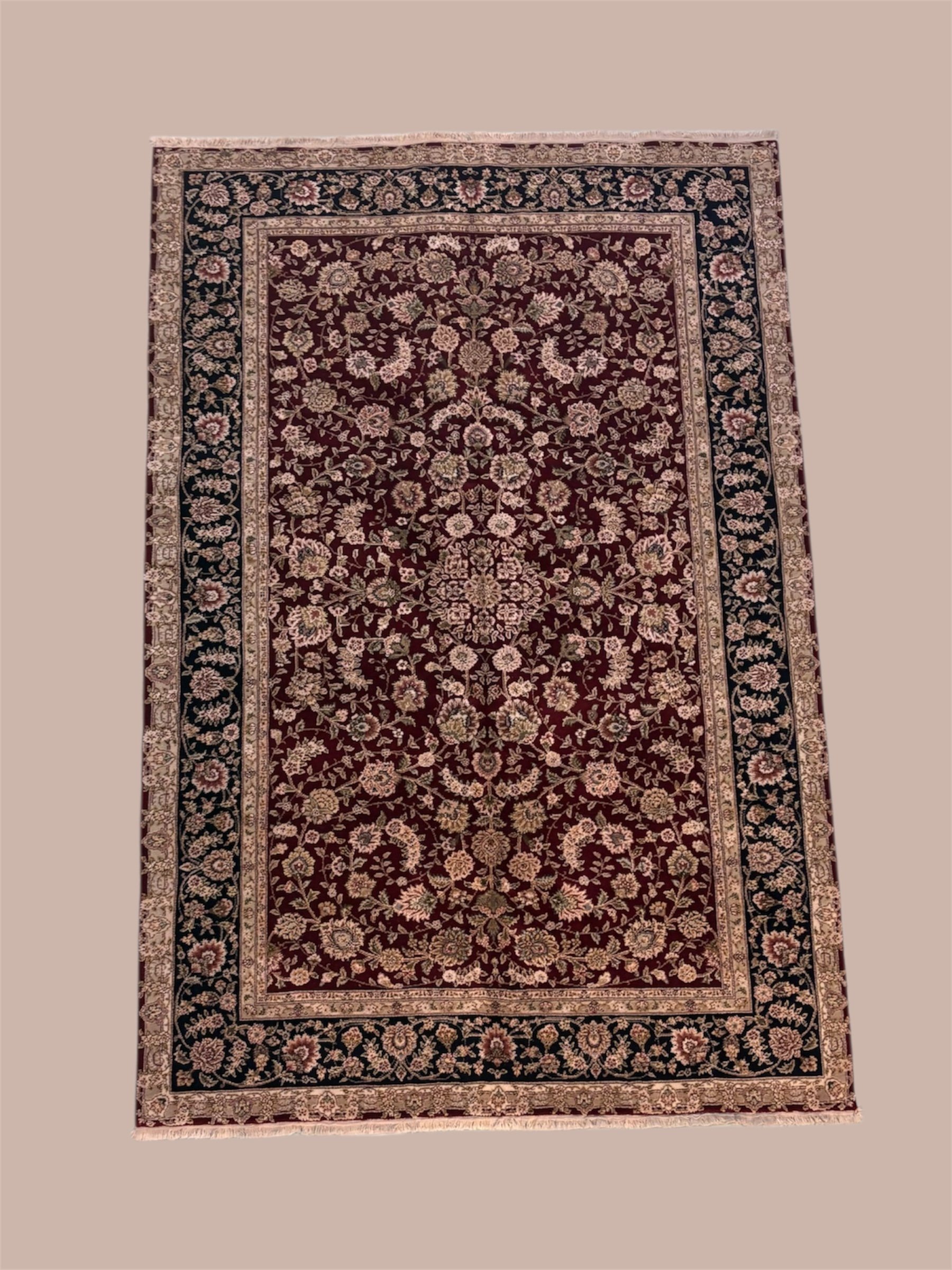 A traditional Persian-style area rug with a deep red background and intricate floral patterns in beige, green, and pink. It features a central medallion and borders with detailed motifs.