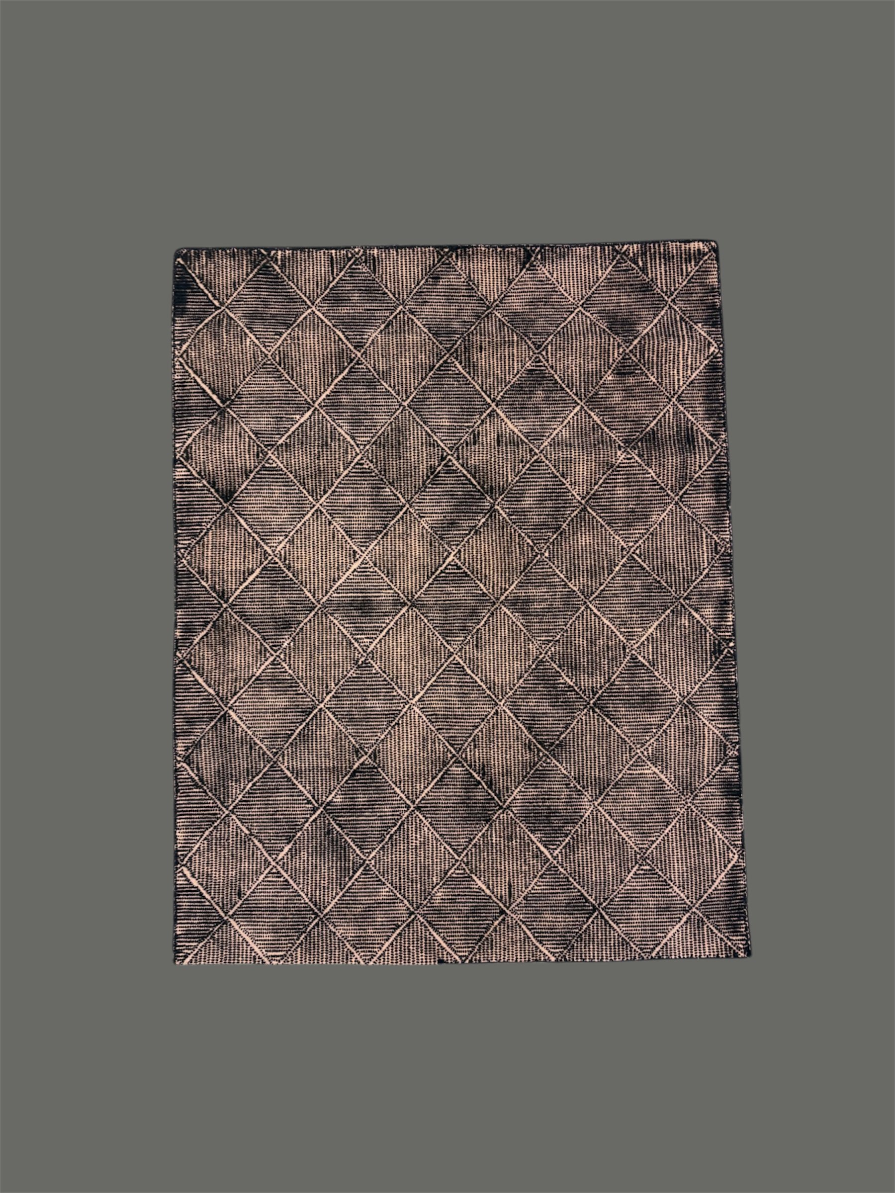 Close-up of a rectangular area rug with a geometric diamond pattern in pink and black tones, laid on a dark grey floor.