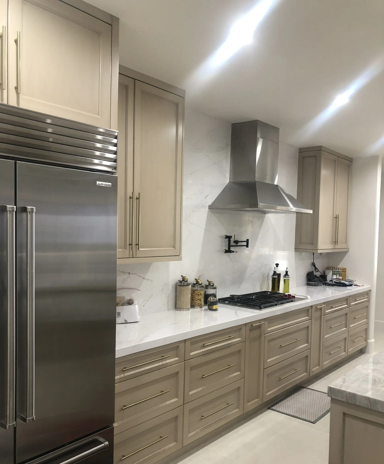 Kitchen with beige cabinets, white marble countertop, stainless steel refrigerator, and stove with a stainless steel range hood.