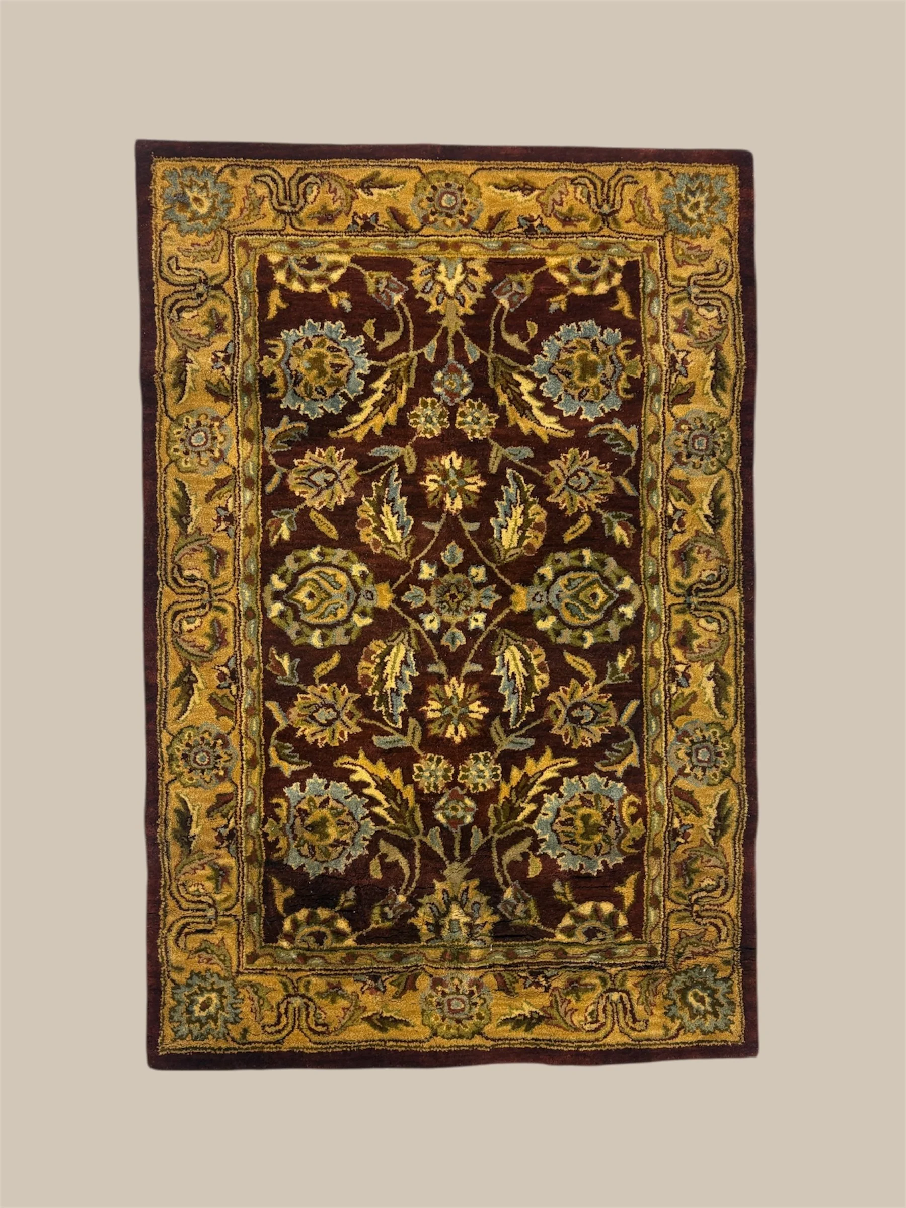 A decorative rectangular area rug with floral patterns in shades of gold, blue, green, and burgundy, bordered by a gold and burgundy design.