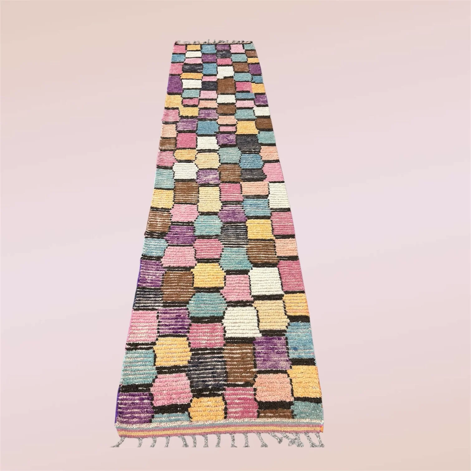 A colorful, patterned rug with a patchwork design of various pastel and earth-tone colors on a light pink background.