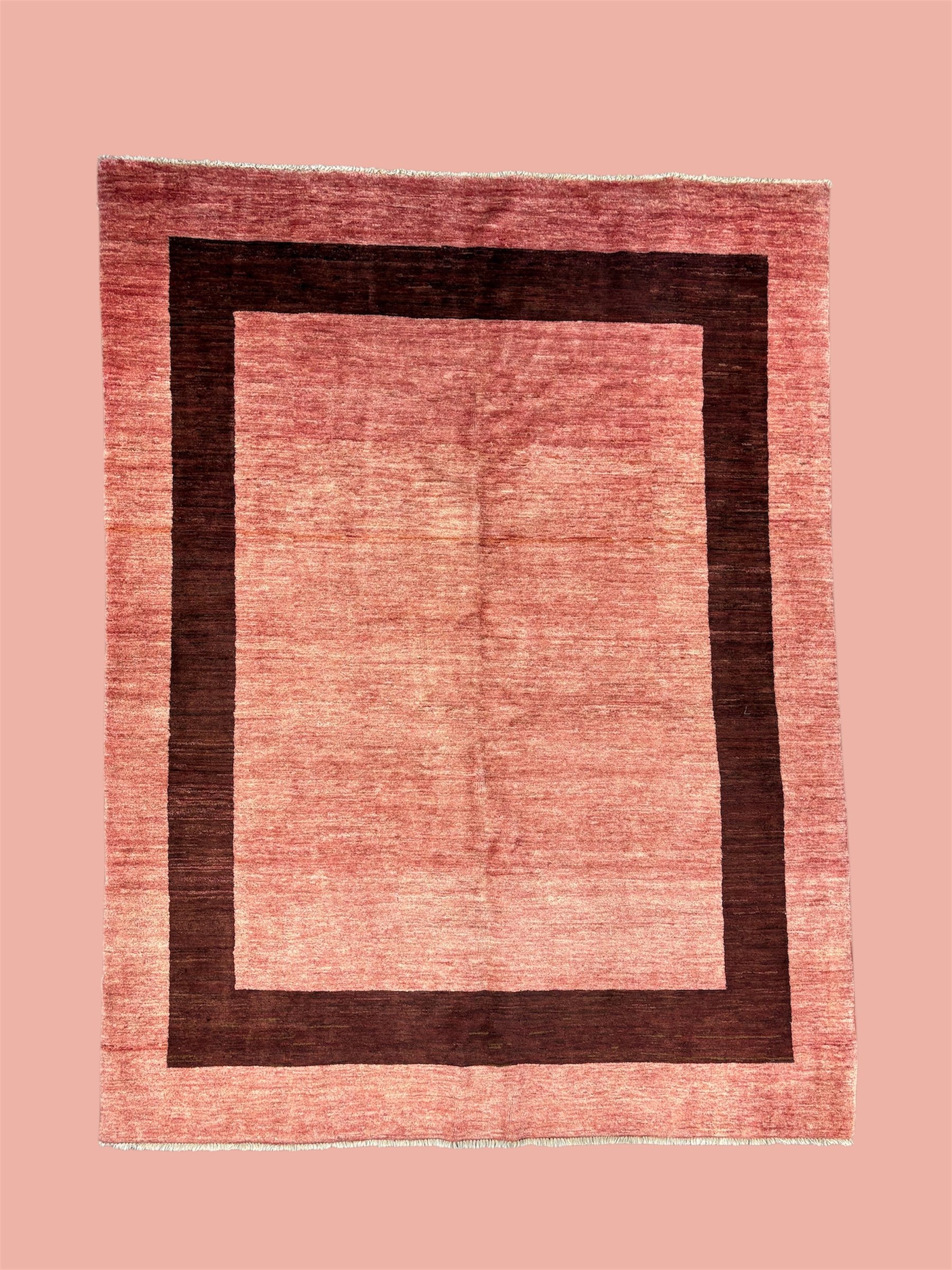 A rectangular area rug with a color gradient from pink to a dark burgundy border, placed on a pink floor.