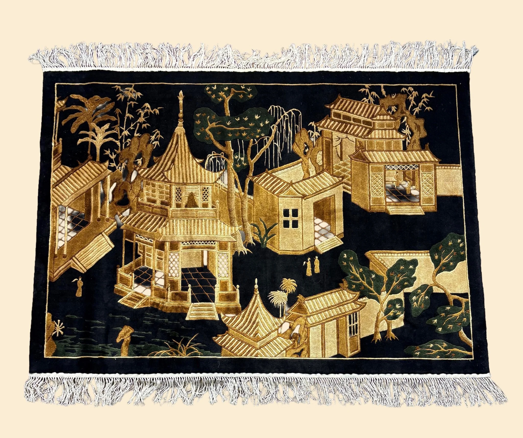 An intricately embroidered textile depicting a traditional Asian scene with buildings, trees, and figures, featuring gold and dark colors.