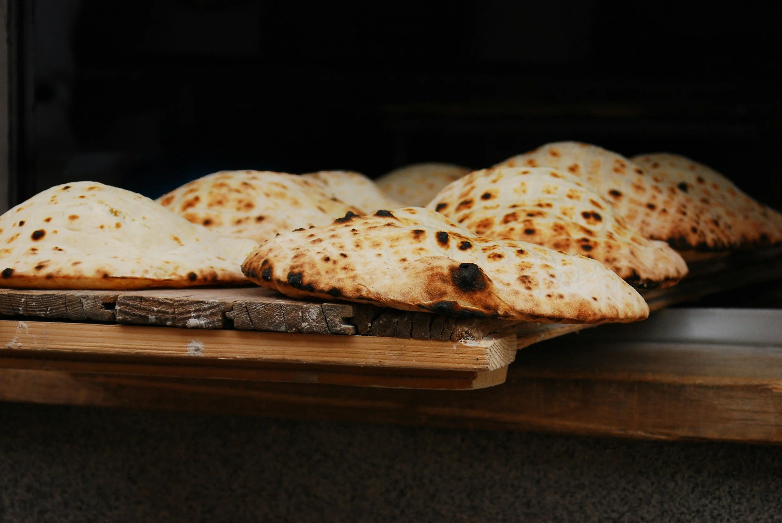 Four freshly baked, slightly burnt flatbreads on a wooden tray.