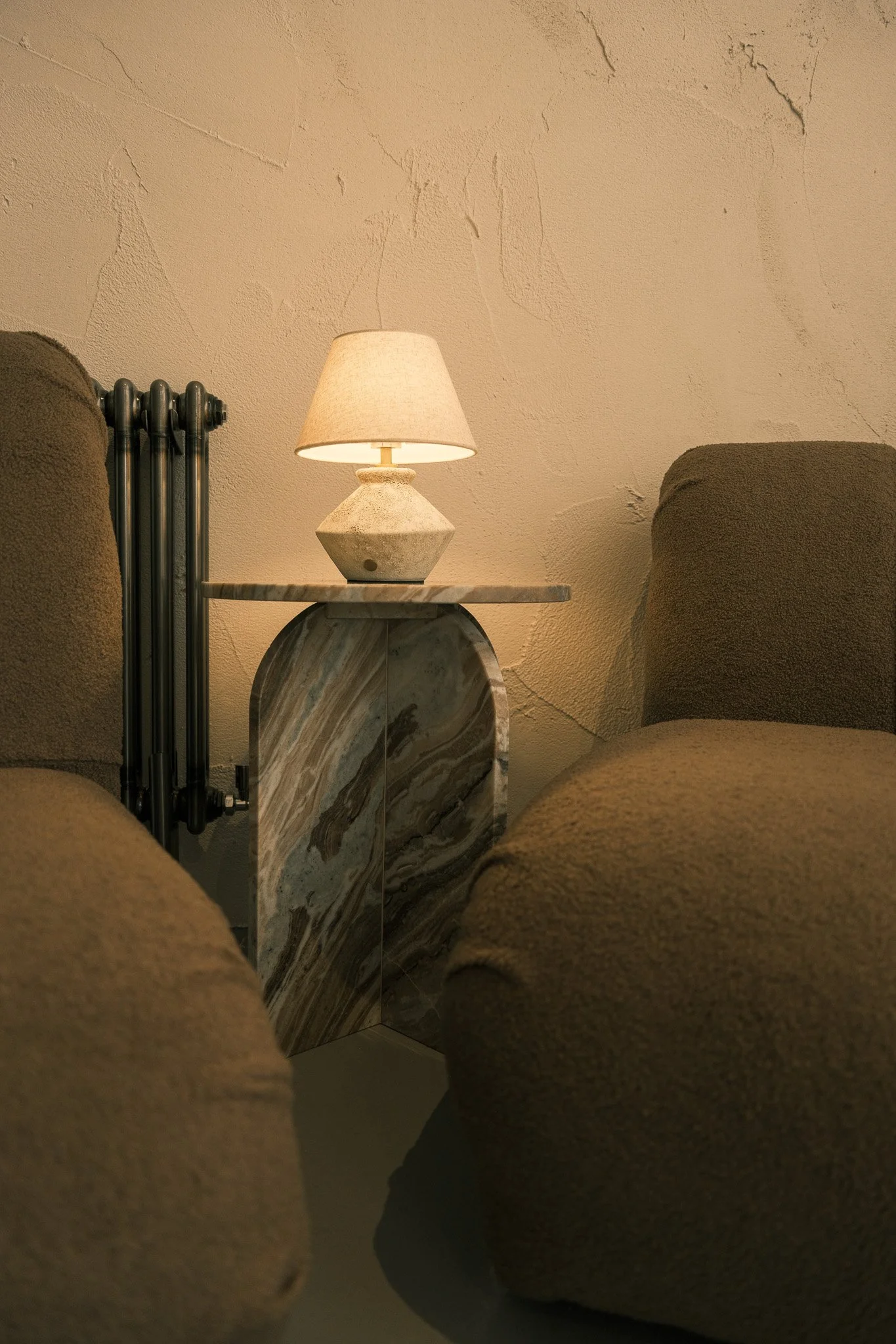 A cozy living room corner with a lamp on a marble side table surrounded by brown upholstered armchairs.