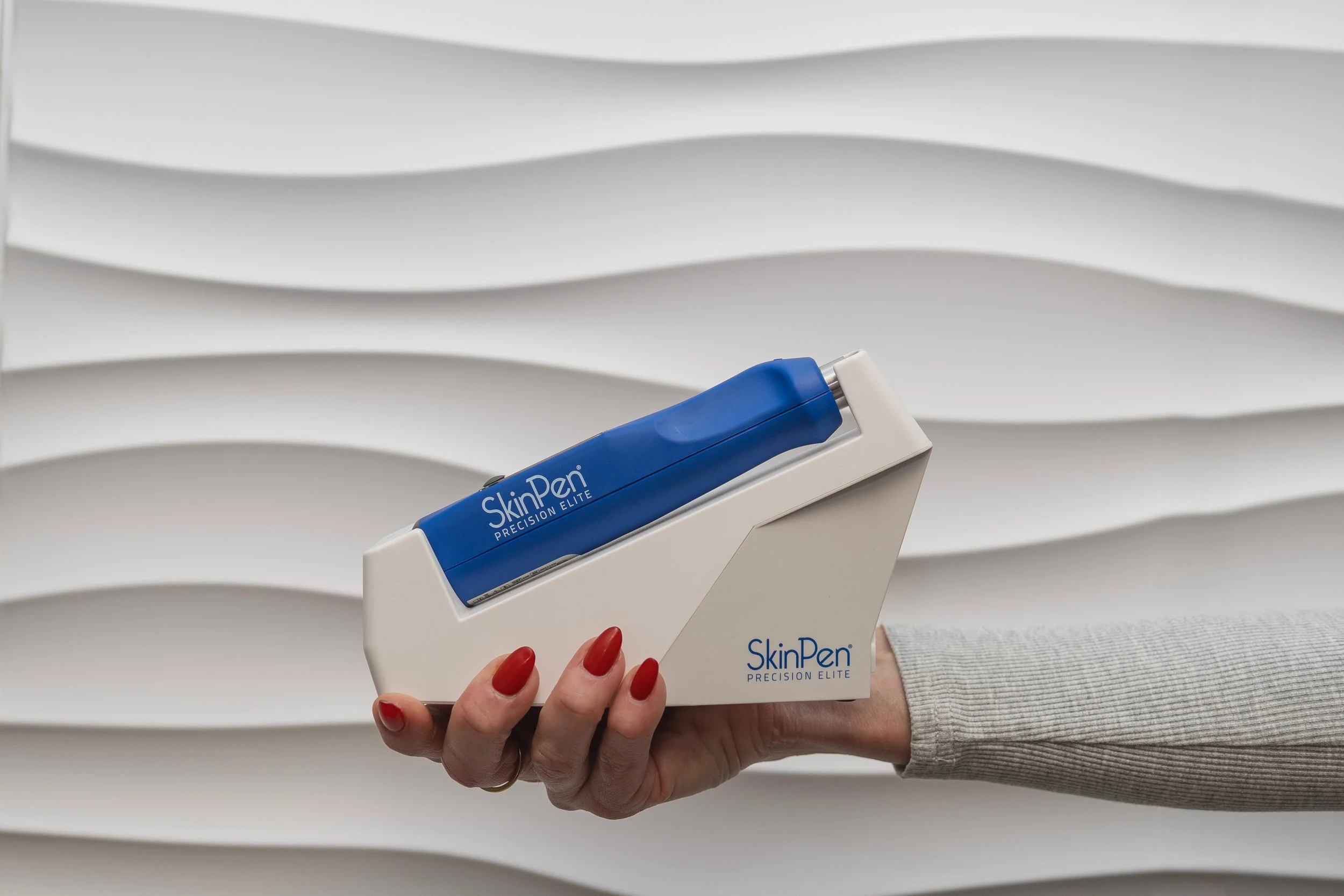 A hand holding a SkinPen device in front of a textured white surface.