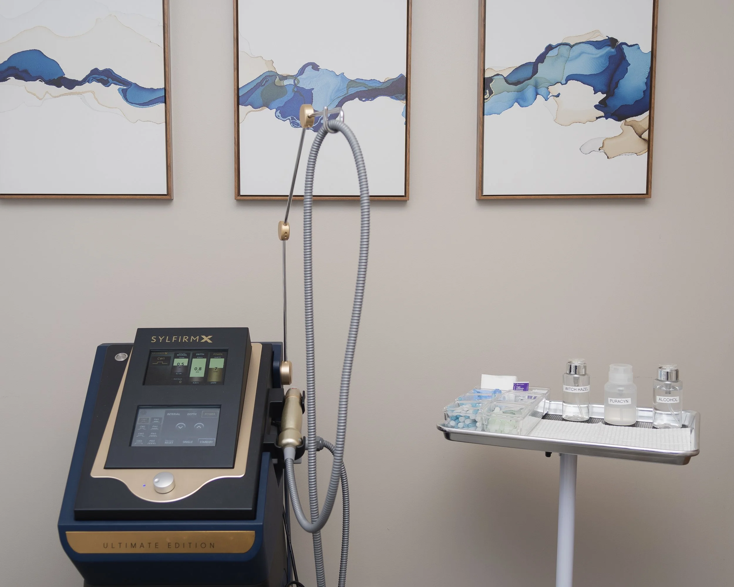 A woman with her eyes closed has her face gently touched by hands wearing black gloves, in a skincare or beauty treatment setting.