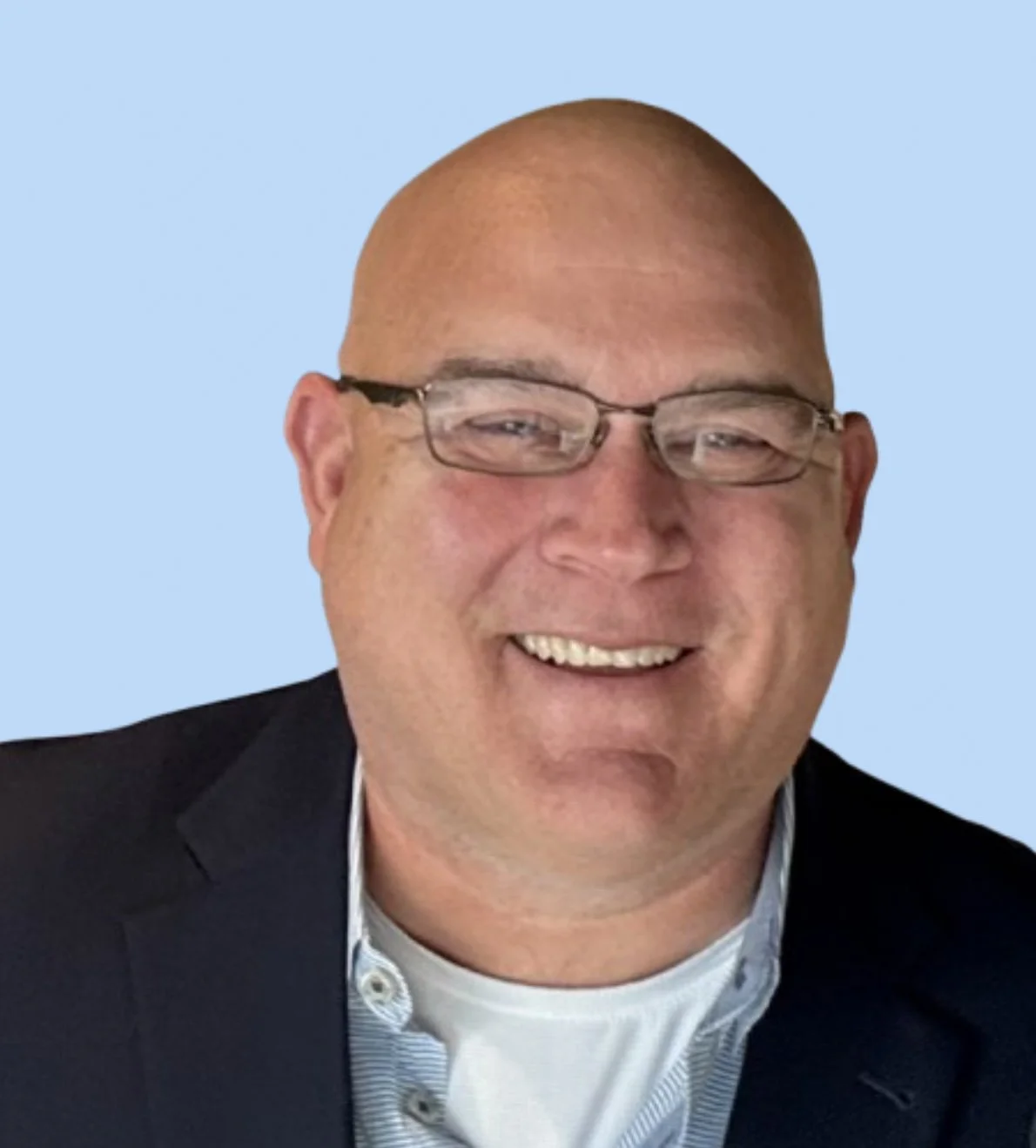A smiling man with glasses, wearing a dark blazer and a collared shirt, against a light blue background.