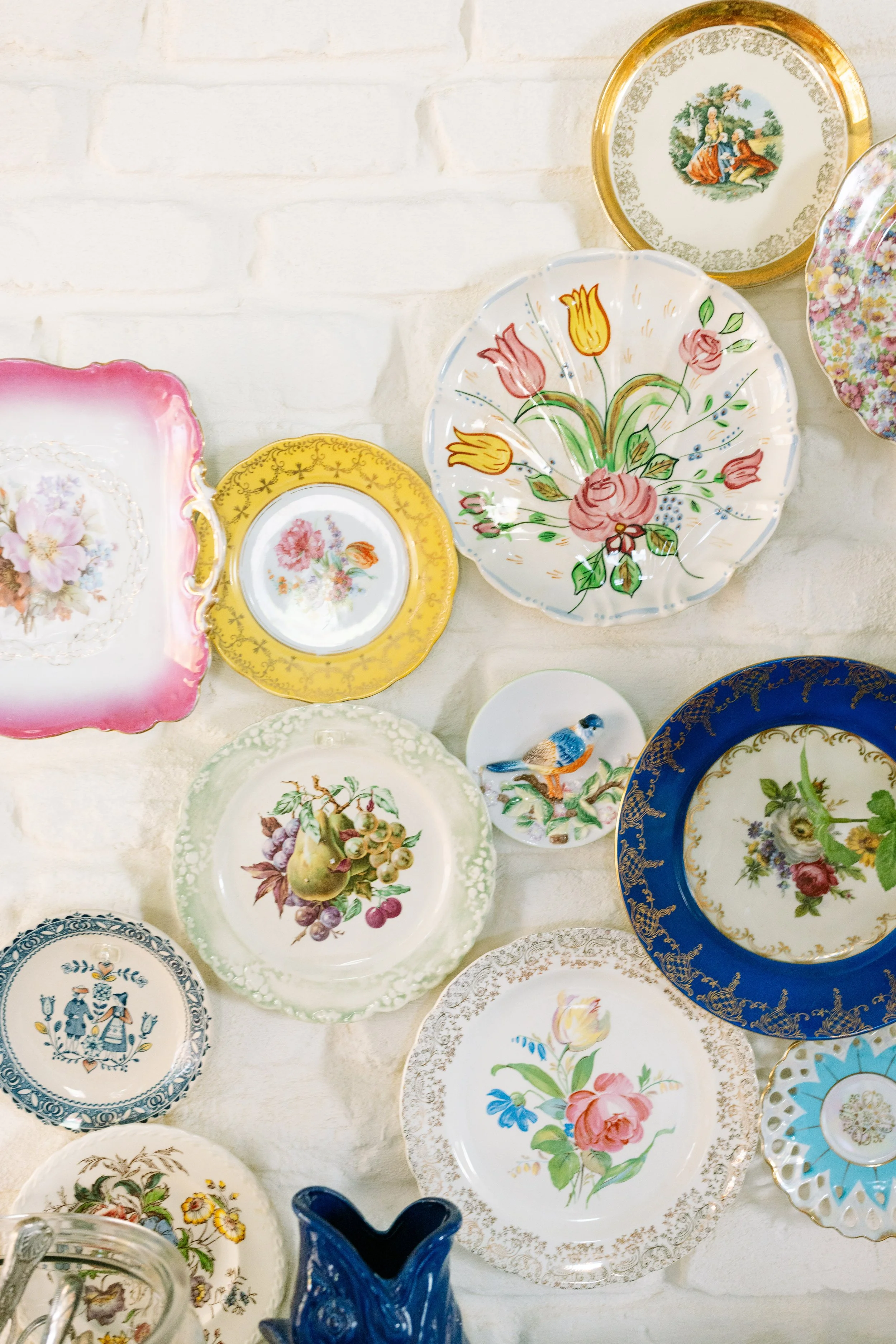 Collection of decorative porcelain plates with floral and fruit designs, displayed on a white surface.