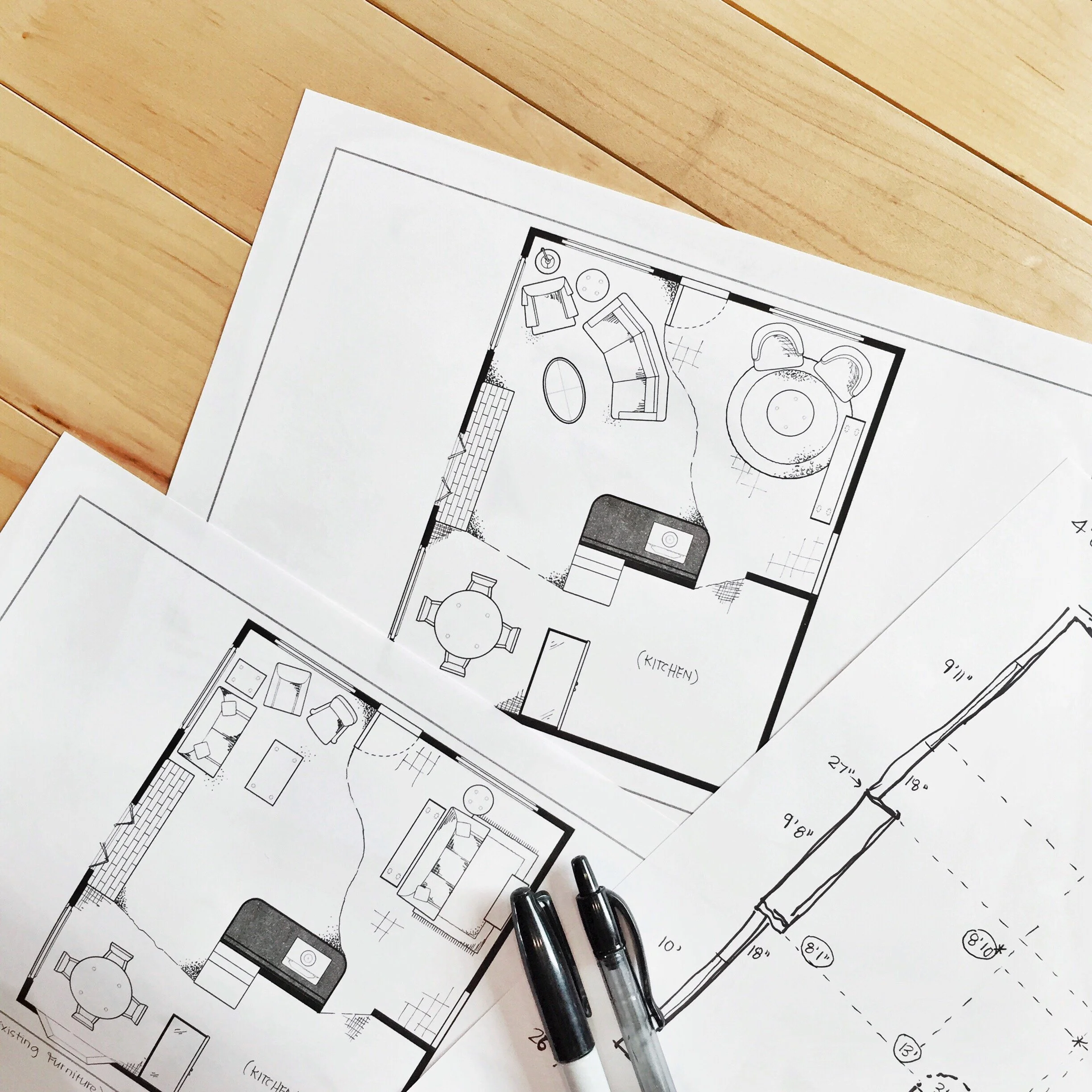 Architectural floor plan documents on a wooden surface with two black pens placed on top.