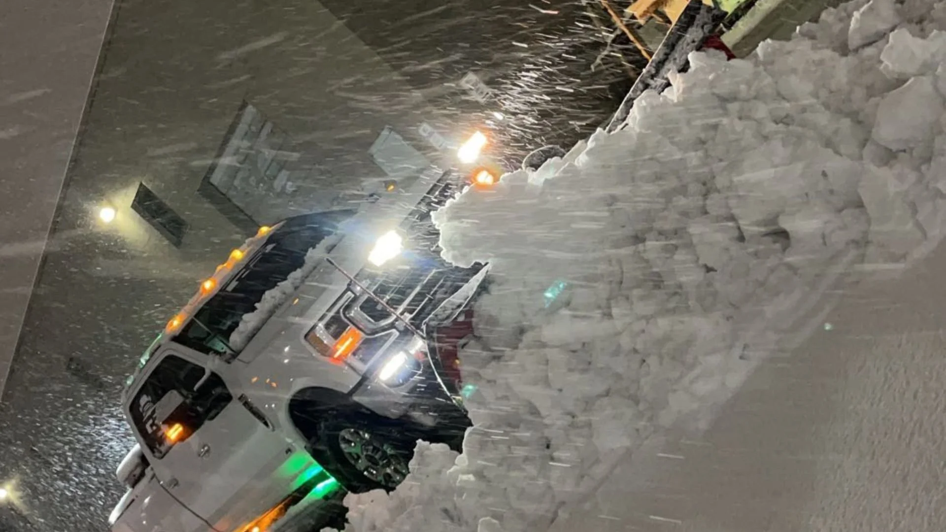 A white pickup truck parked outside in snowy weather at night with snow falling heavily.