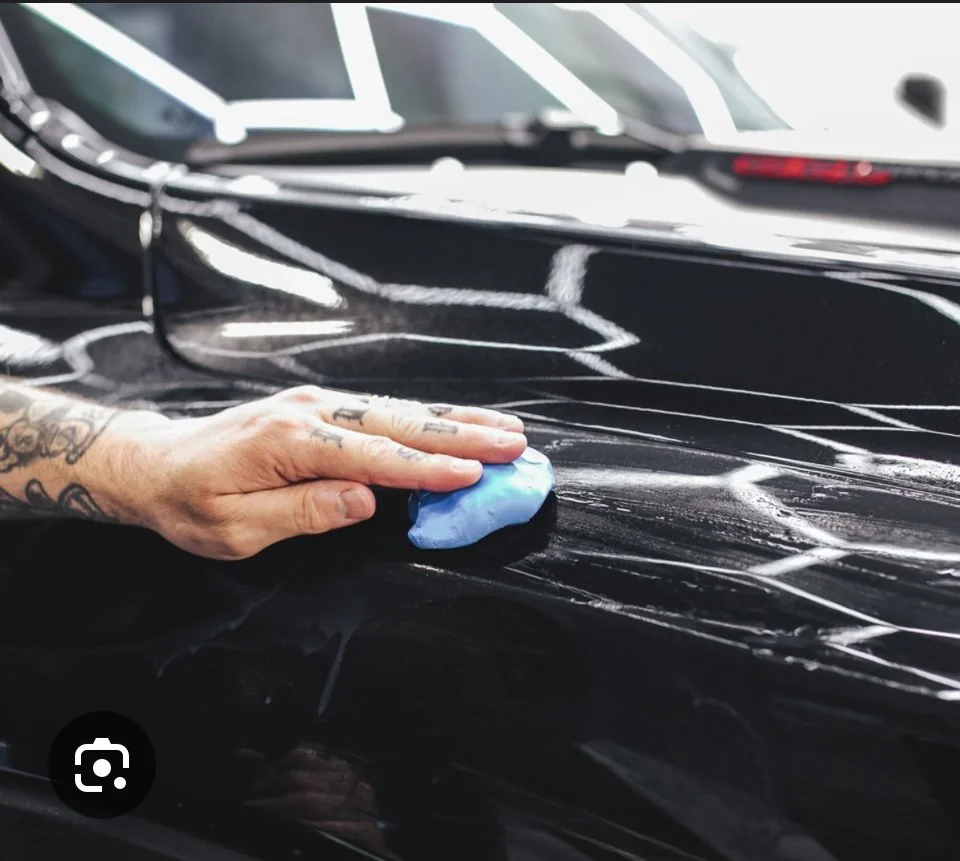 Professional clay bar treatment process removing embedded contaminants and surface bonded particles from black vehicle paint during mobile car detailing service