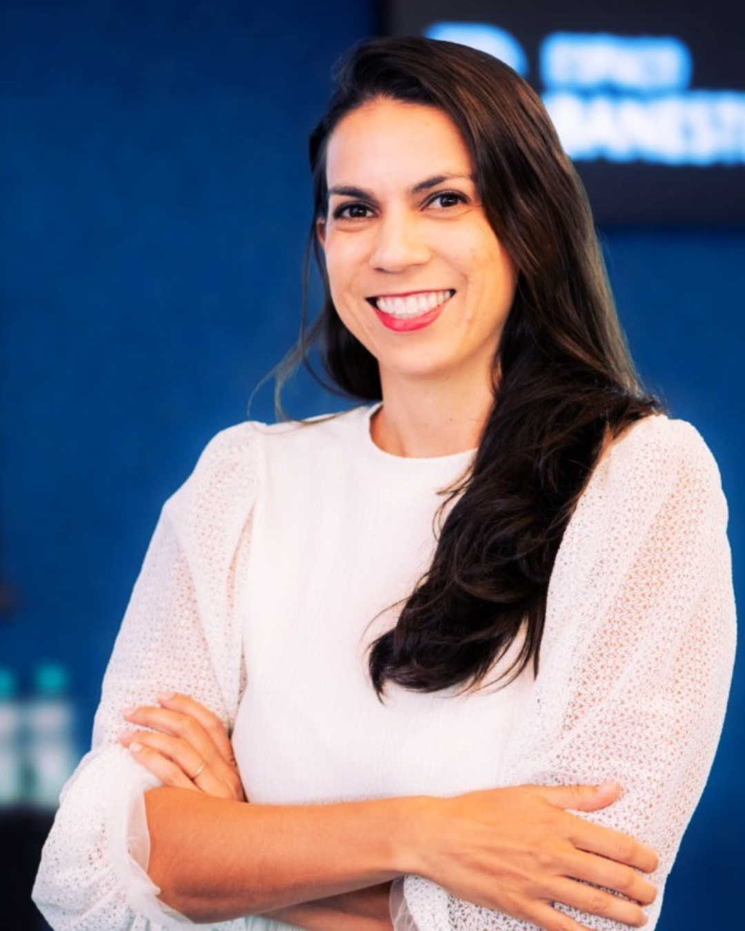 Julia Caiado, CEO da Global Touch, com cabelos lisos escuros soltos vestindo uma blusa branca de braços cruzados e sorrindo