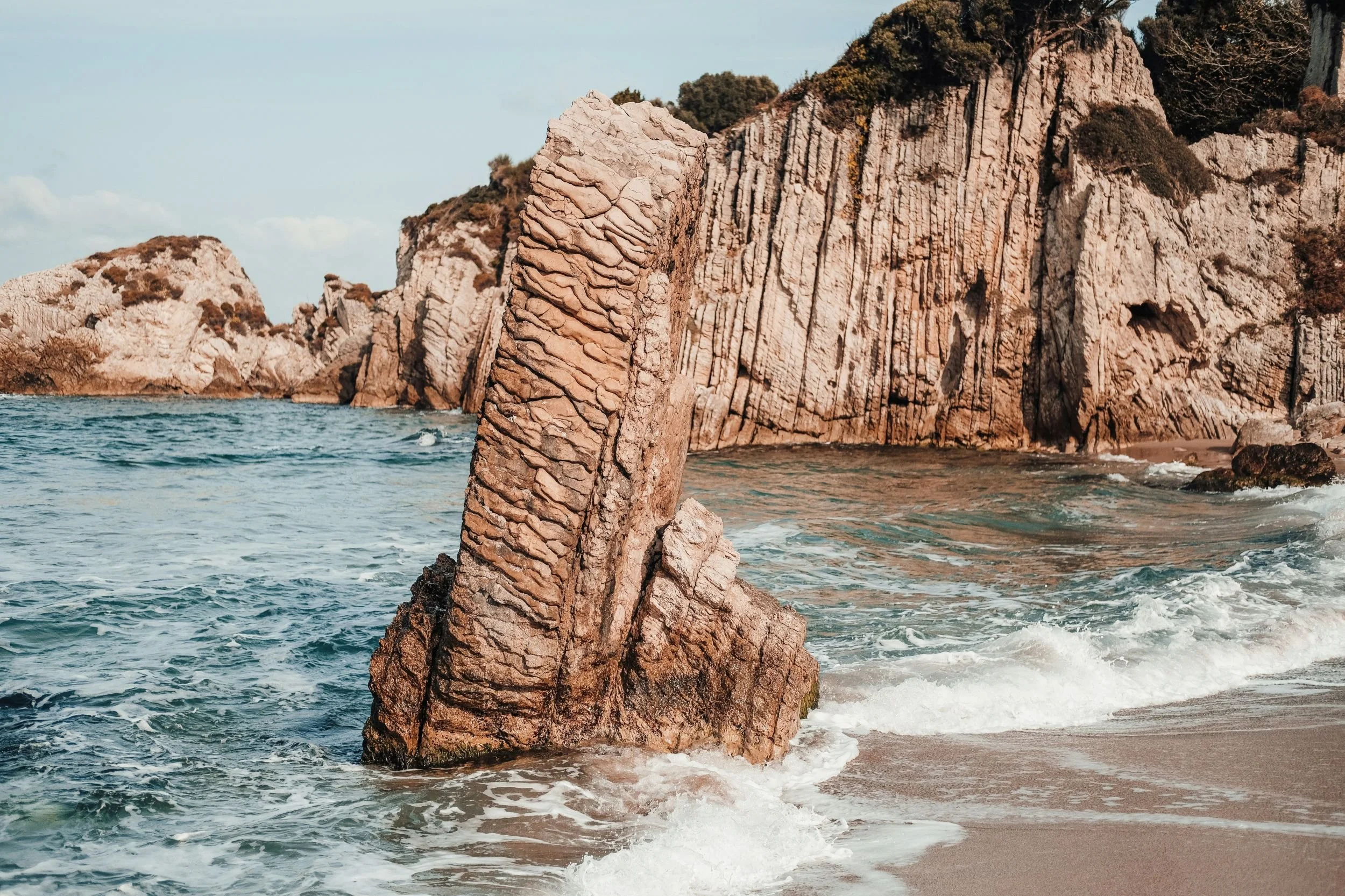 Sand coloured rock on a beach surrounded by cliffs and waves
