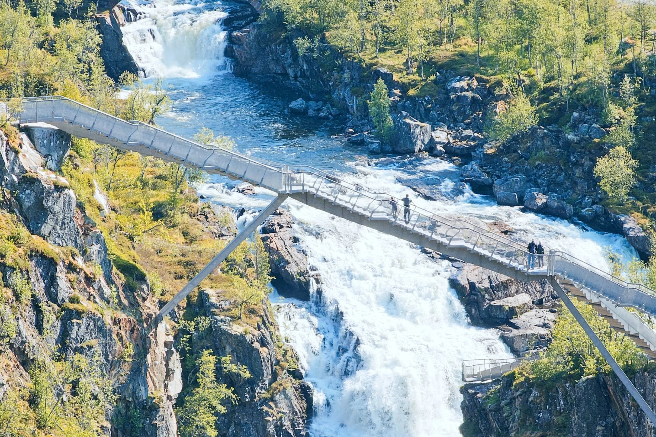 Metal stairway over a large waterfall with people standing on it.