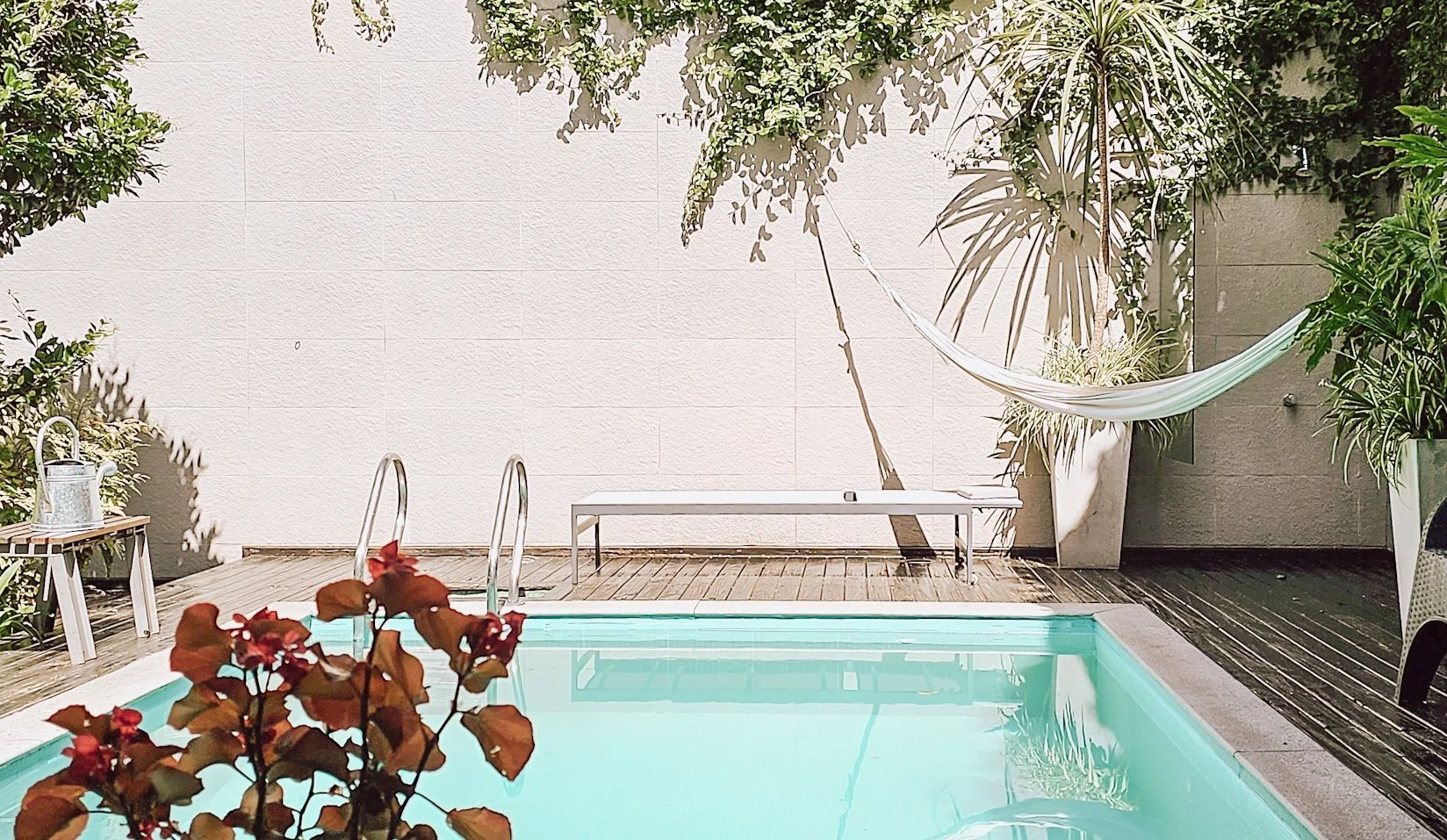 Intimate courtyard with a single white hammock hanging near a pool with pale blue water.