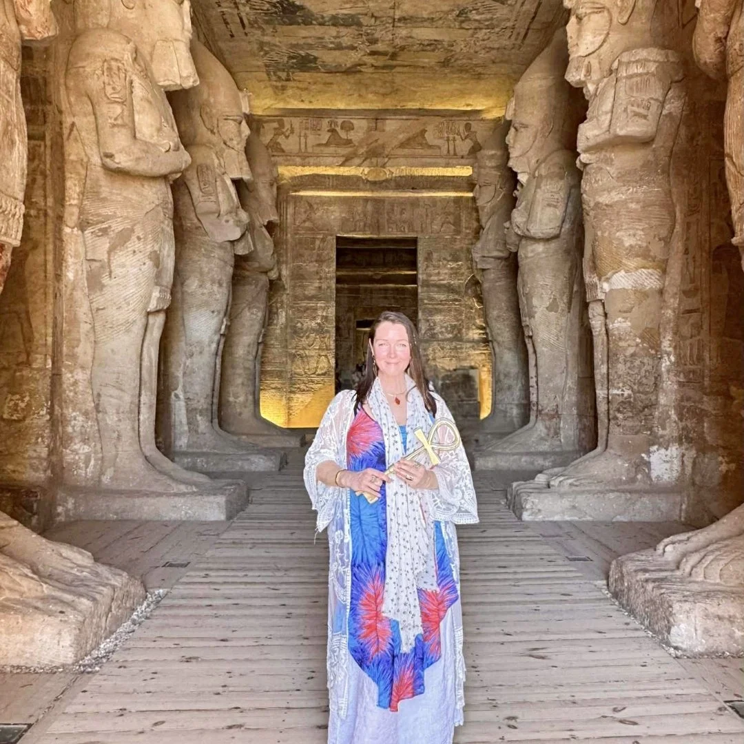Female in a colourful dress standing in the entrance of an Egyptian monument with large statues on either side