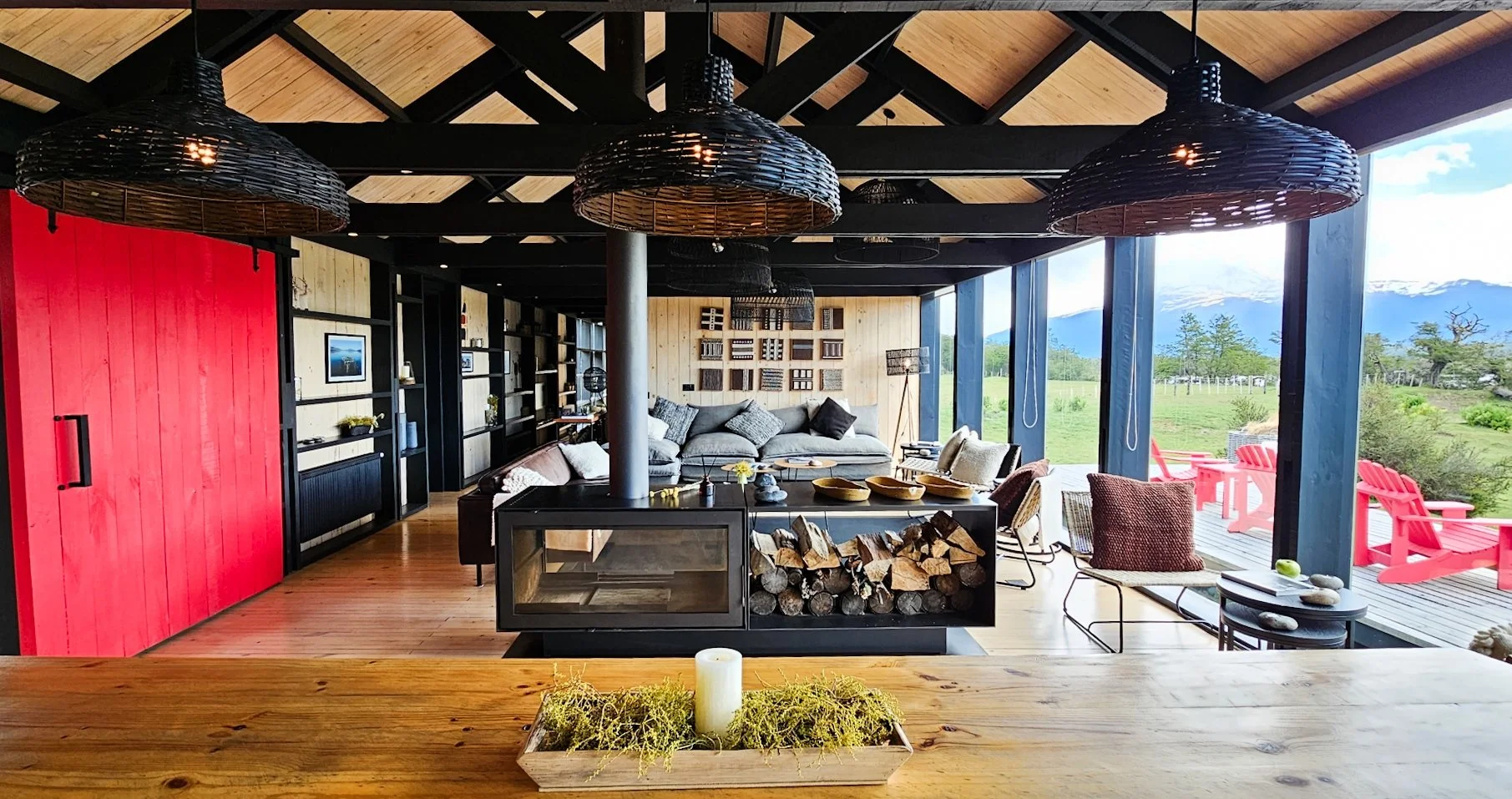 Stylish and cozy lodge with a red barn door, wood burning fire place in the center of the room, sofas, floor to ceiling windows with views of nature.