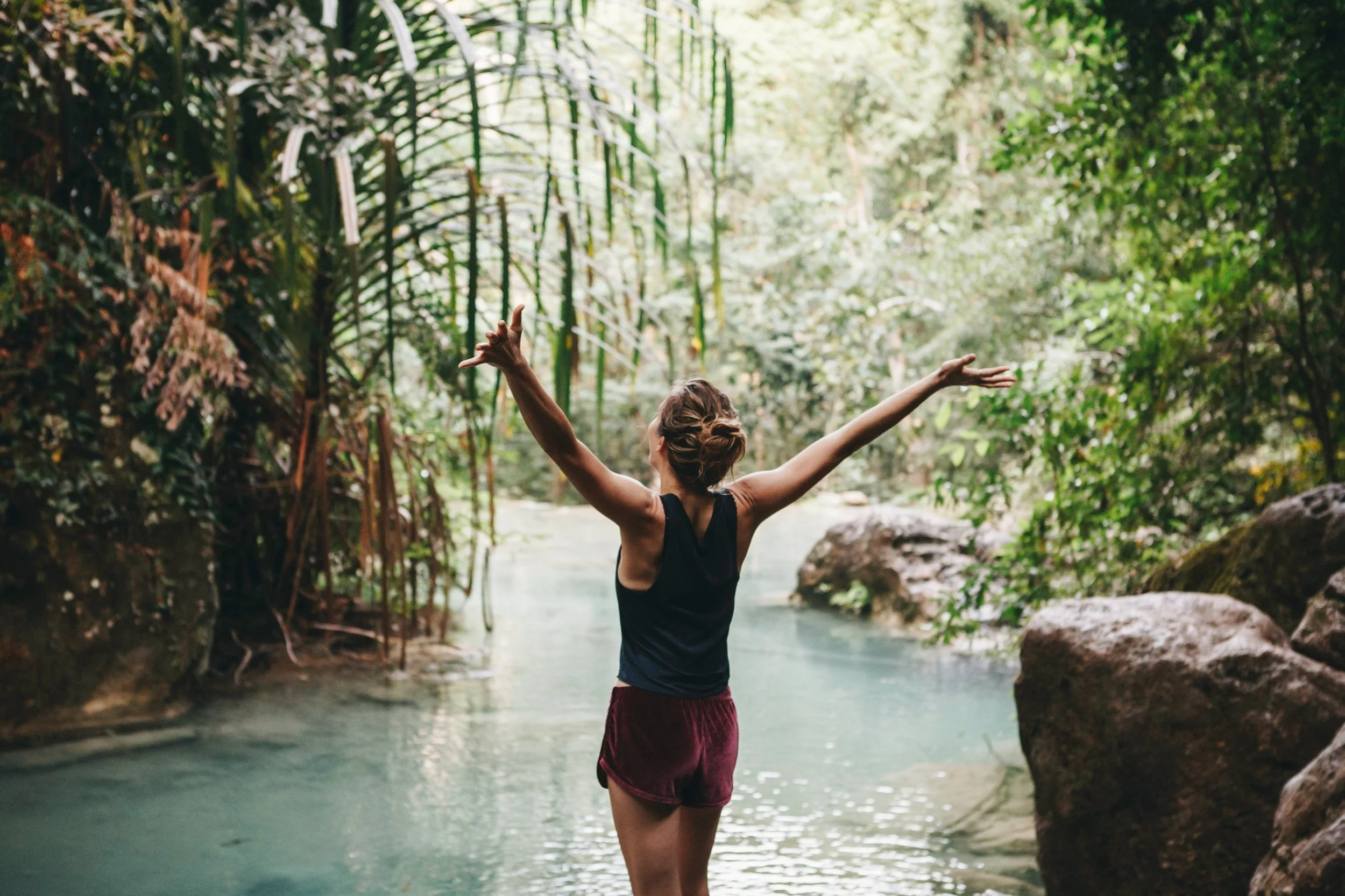 Single female standing in a light blue river surrounded by a green jungle