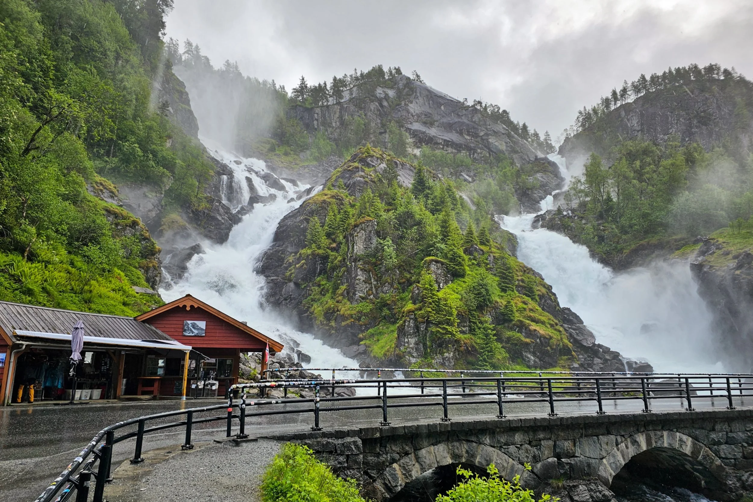 Two large waterfalls cascading down a mountain side beside a road.