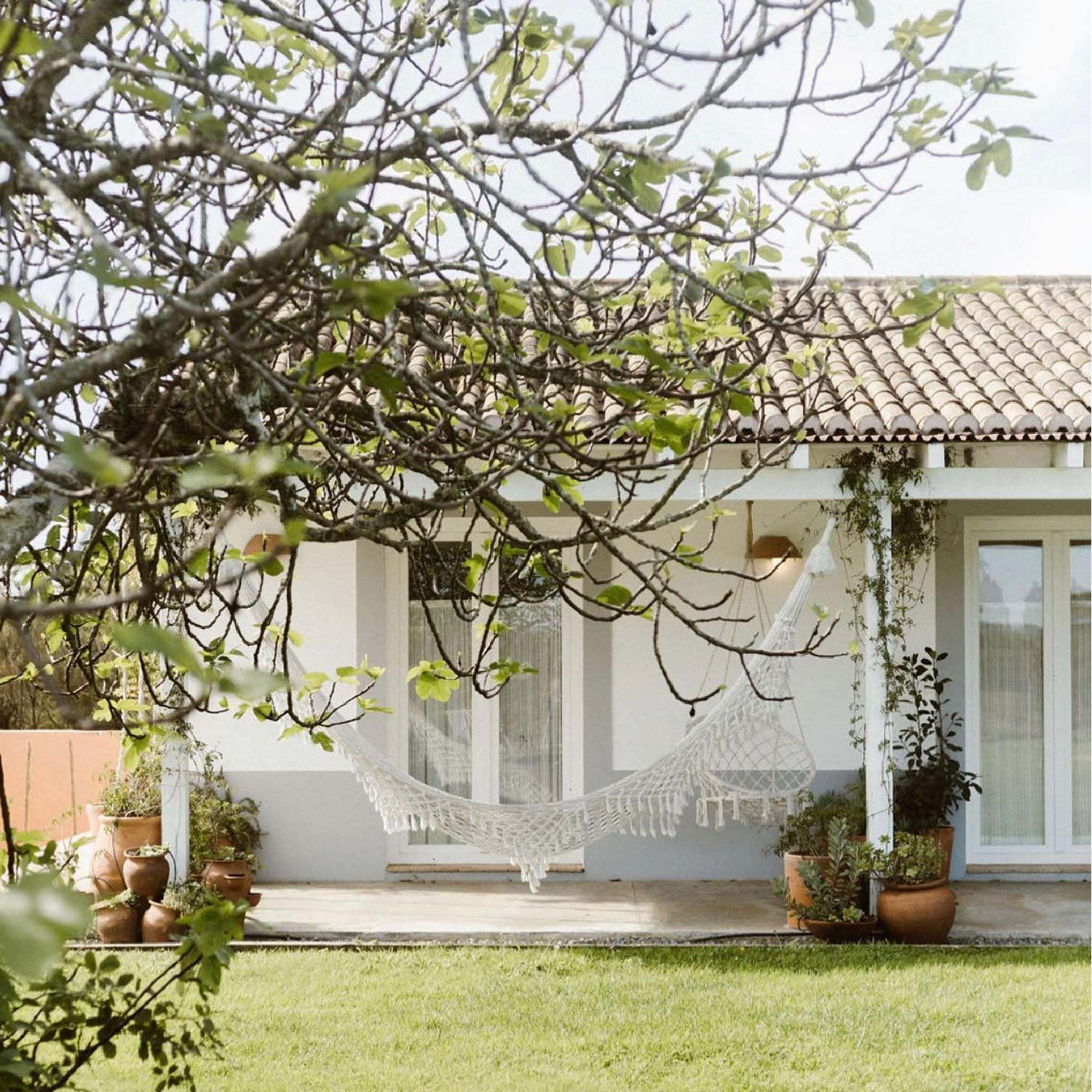 A white hammock on the shaded terrace of a bungalow overlooking a green garden