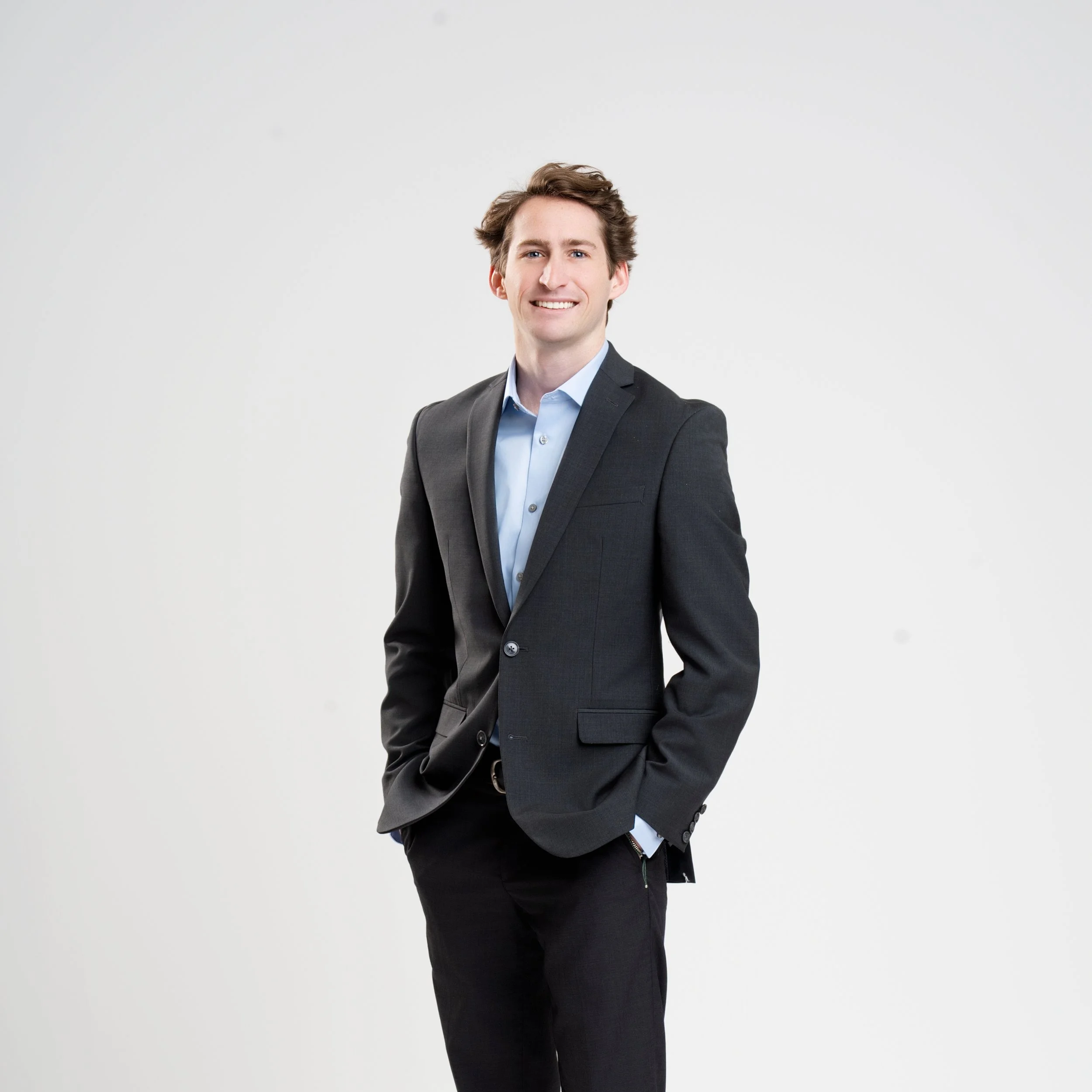 Portrait of a young man in a business suit smiling against a plain white background.