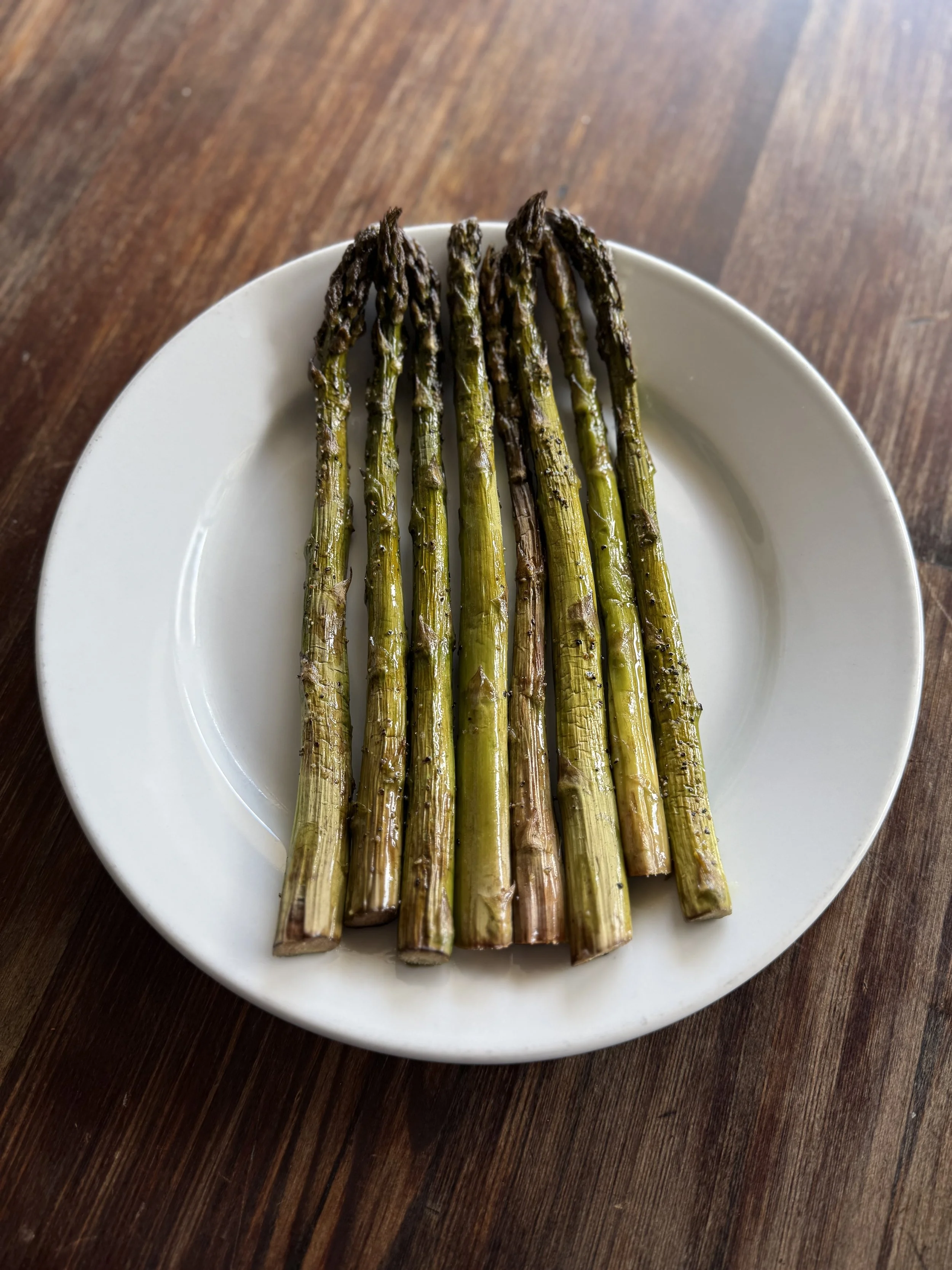 Grilled asparagus spears on a white plate placed on a wooden table.