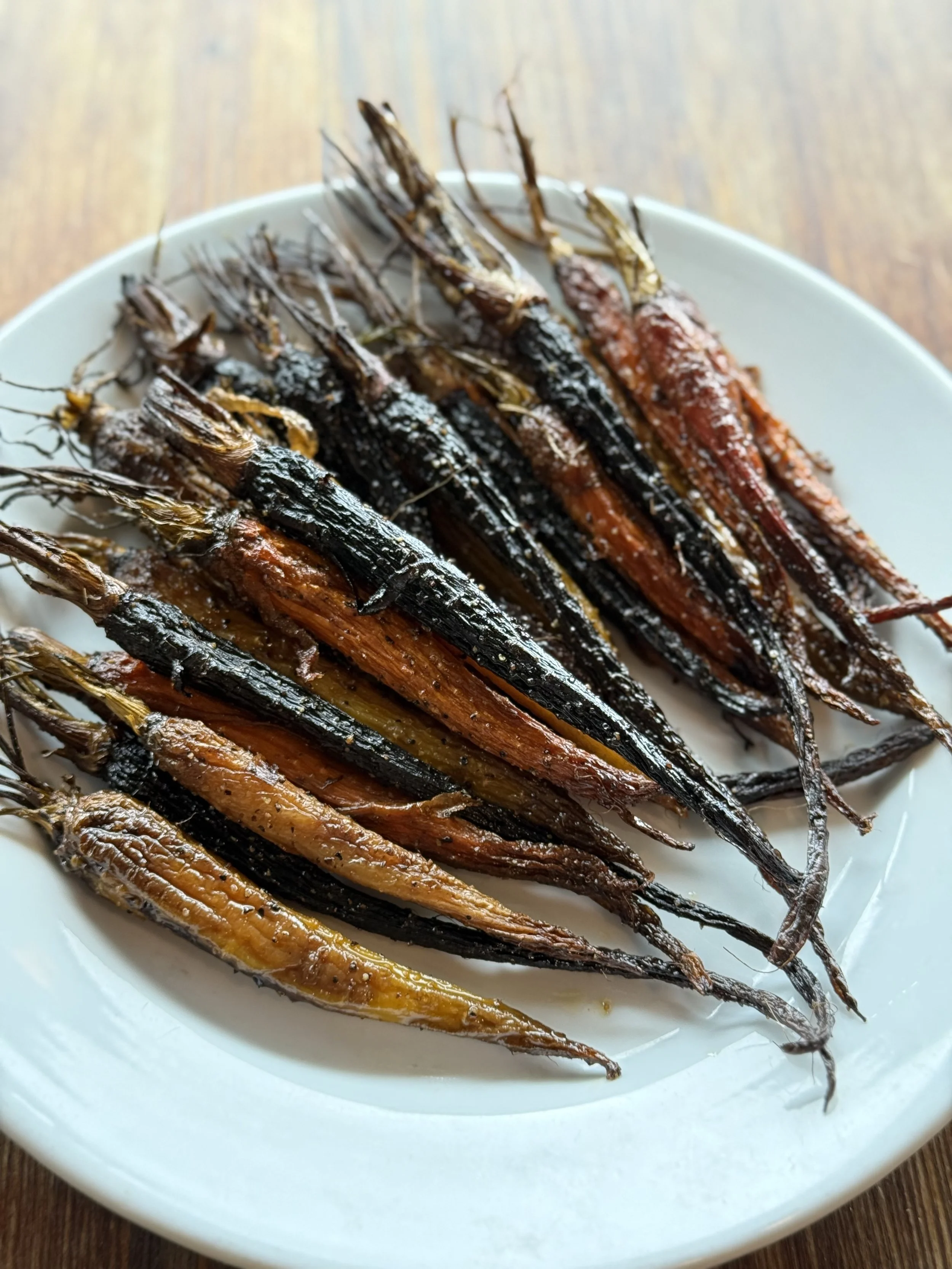 A white plate with roasted small fish, possibly sardines or anchovies, on a wooden table.