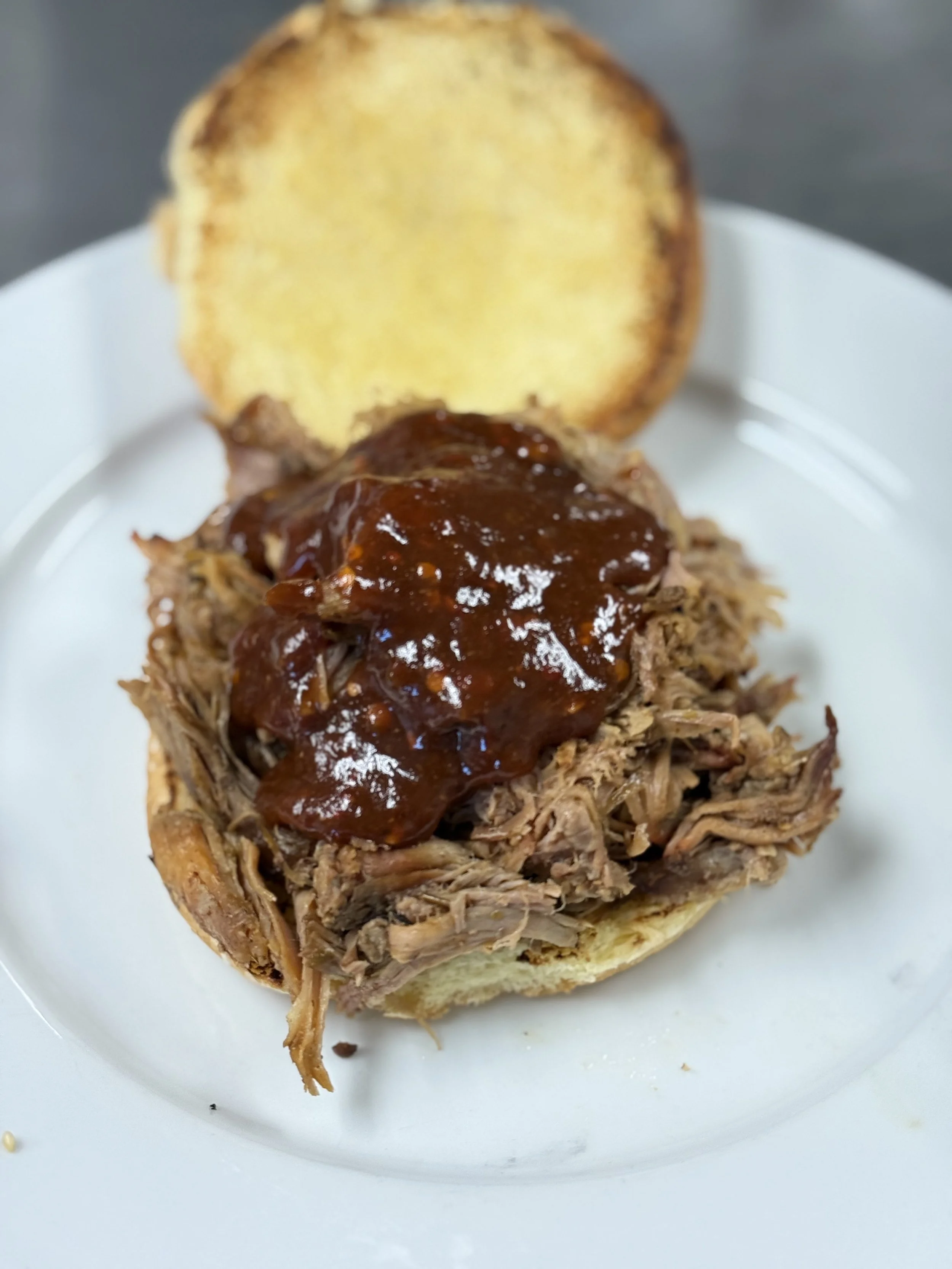 Pulled pork sandwich with barbecue sauce on a burger bun on a white plate.