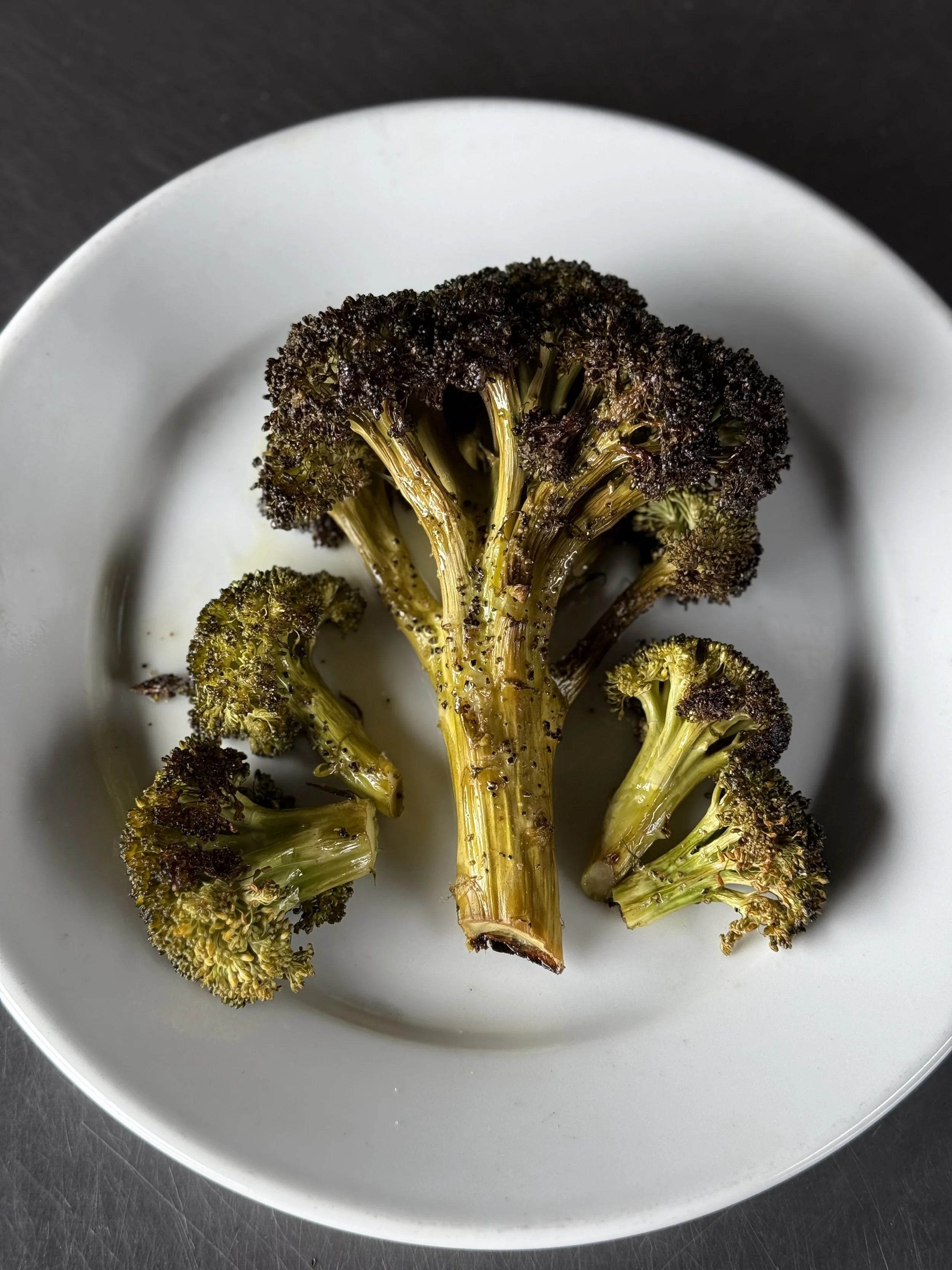 Roasted broccoli florets on a white plate.