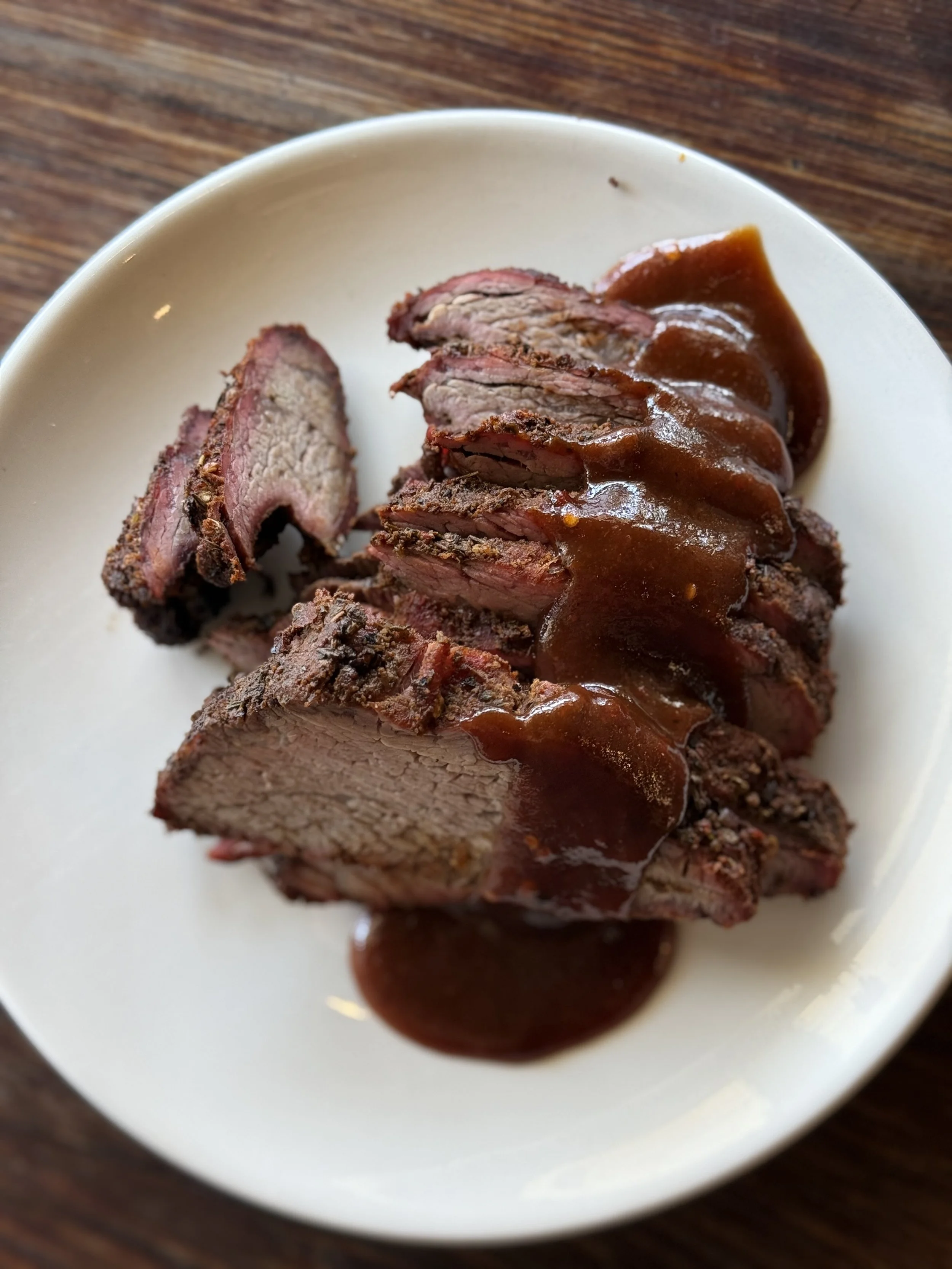Slices of cooked beef topped with rich brown gravy on a white plate, on a wooden table.