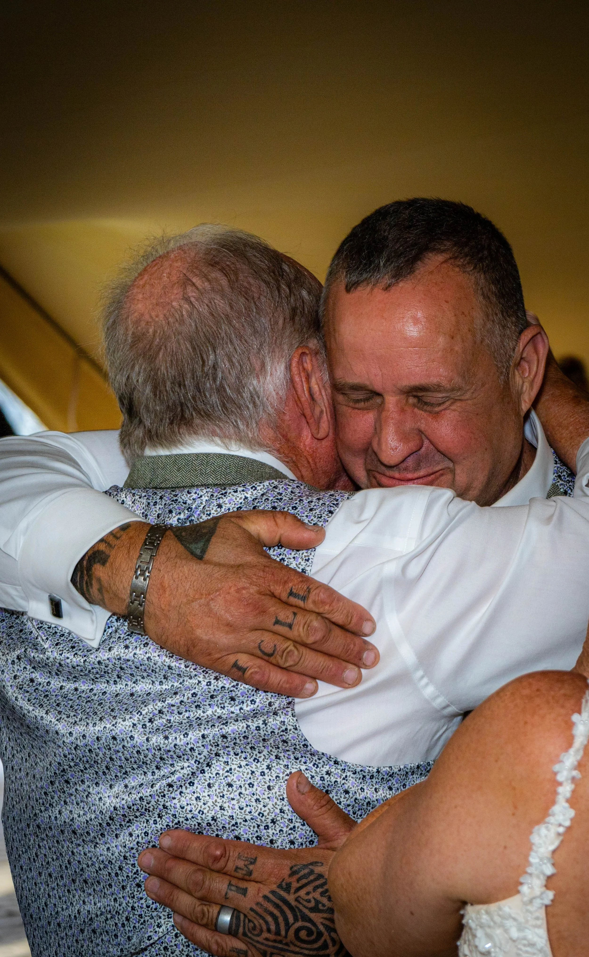 Two men hugging tightly, smiling with their eyes closed, embracing warmly.
