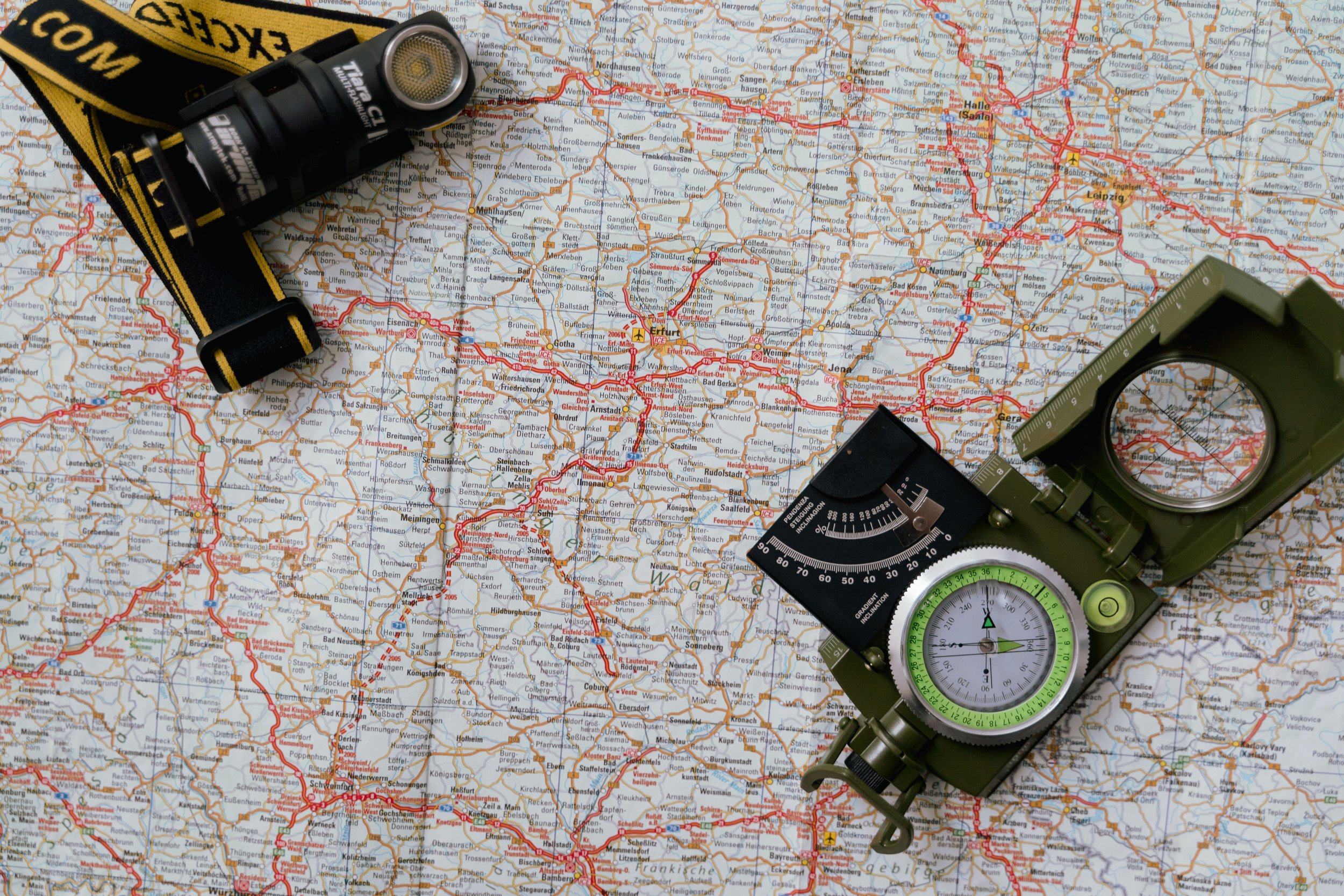 A detailed map of central Germany, with a black and yellow headlamp, a green compass, and a green military-style map inclinometer placed on top of it.