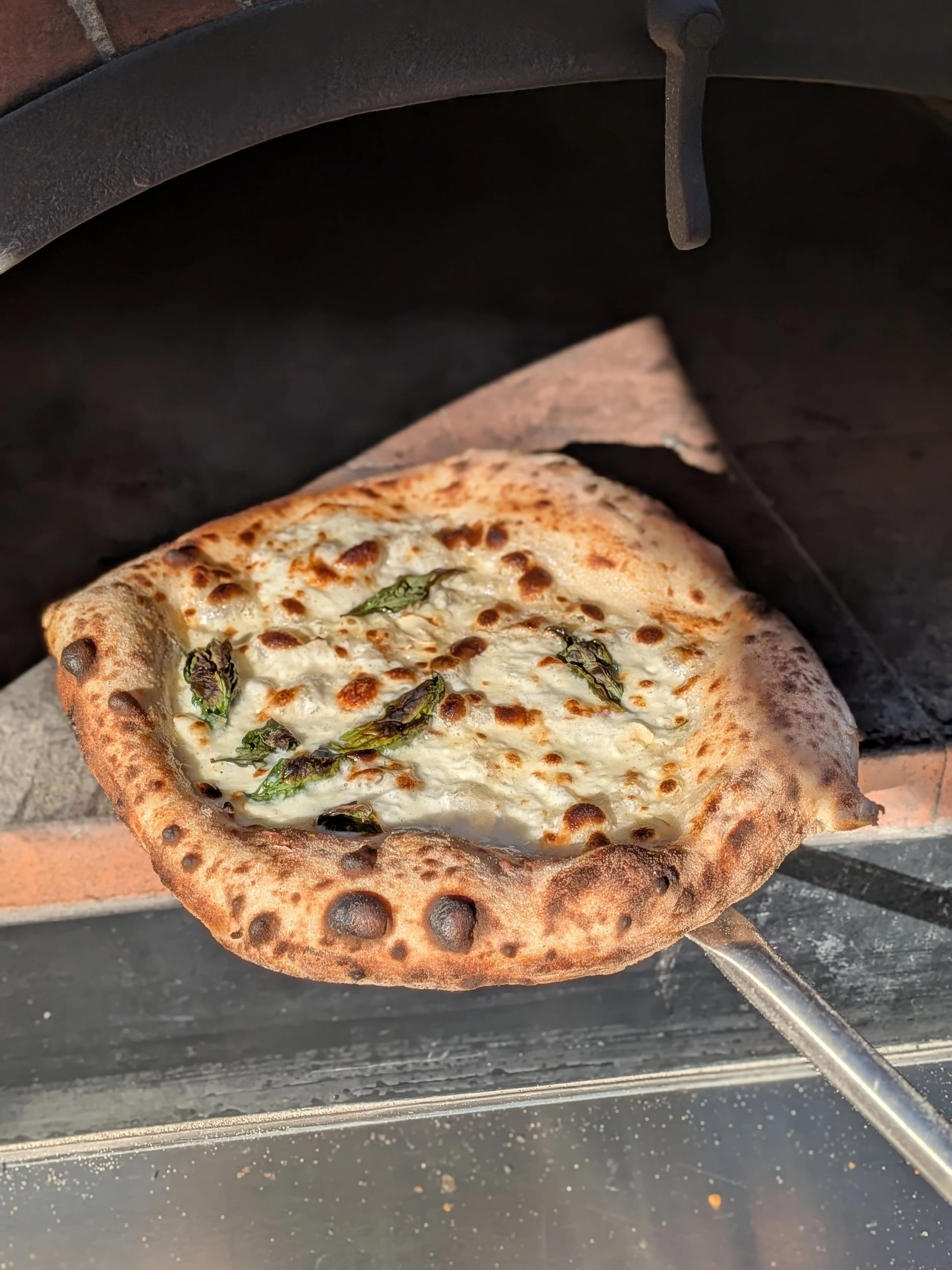 A pizza with cheese and basil cooking in a traditional pizza oven.
