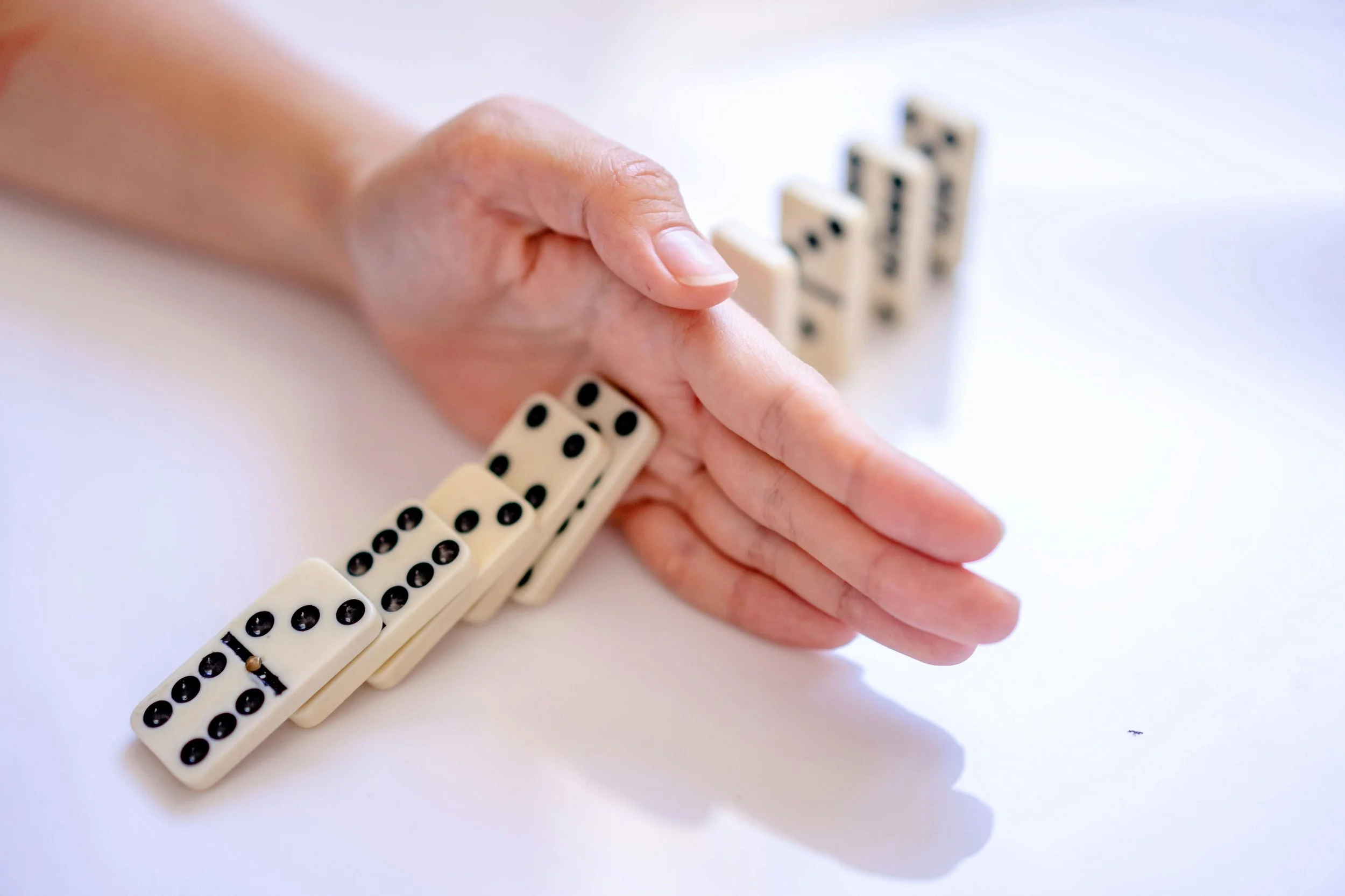 Hand stopping falling domino tiles, symbolizing feeling stuck, breaking patterns, and taking control of stress and mental health