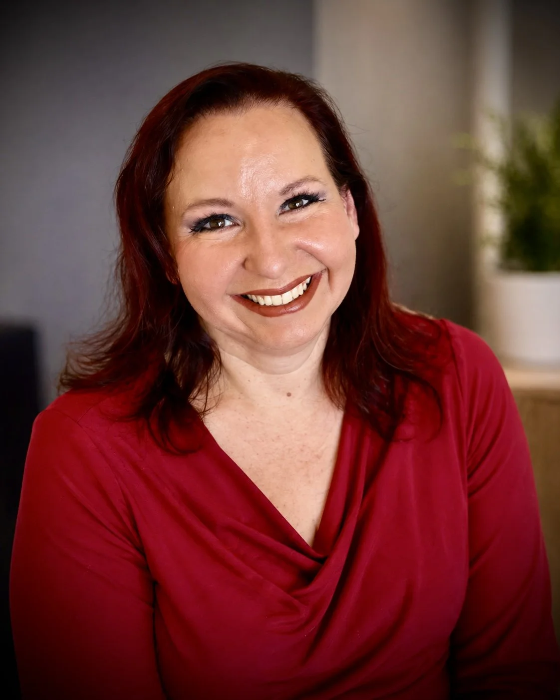 Image of Lisa Johnson, LPC. A licensed counselor. A woman with shoulder-length reddish-brown hair, wearing a sleeveless floral dress, sitting on a beige armchair in an indoor setting, smiling at the camera.