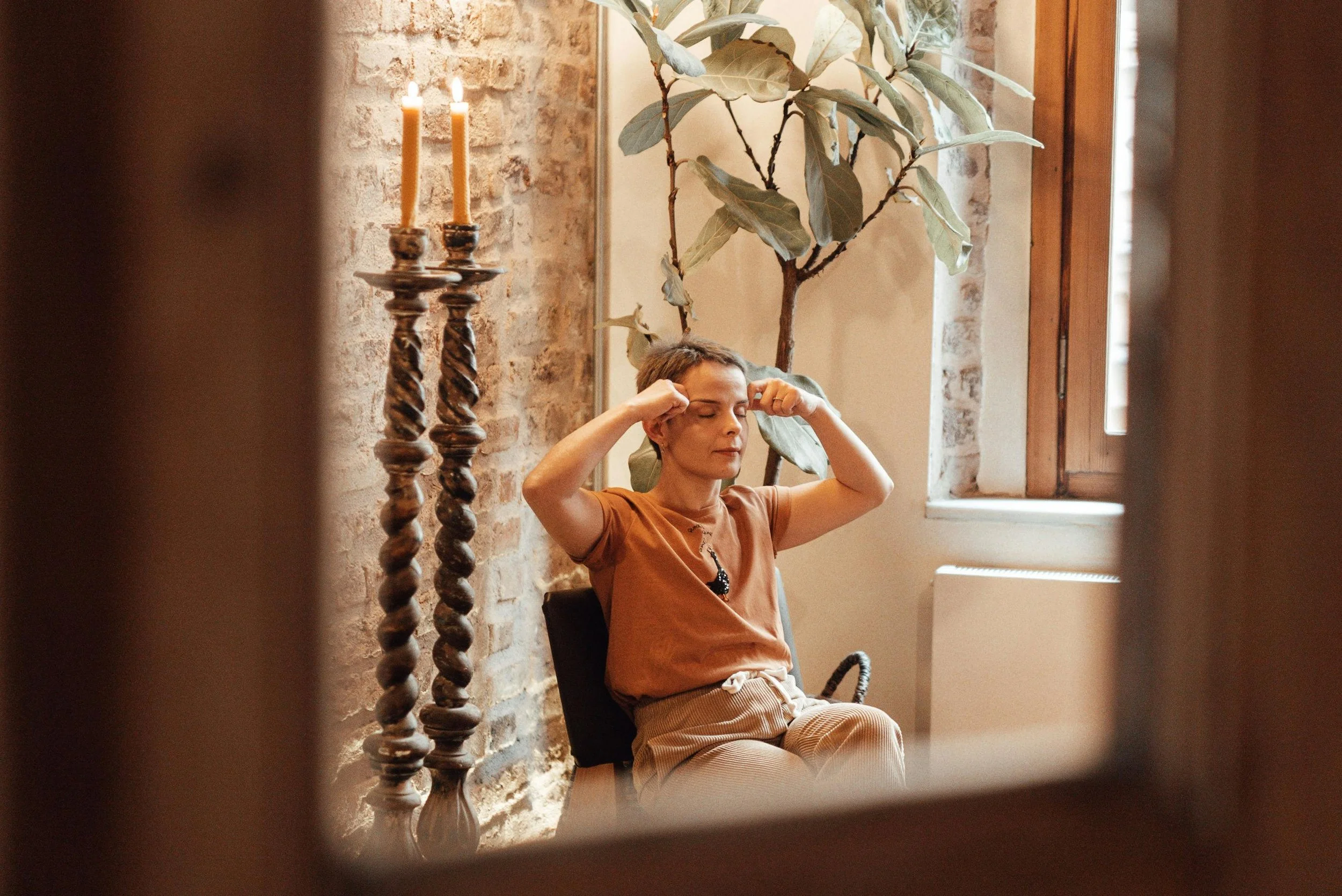 Woman experiencing stress or emotional tension, sitting by a window with eyes closed, illustrating the impact of trauma on mental health