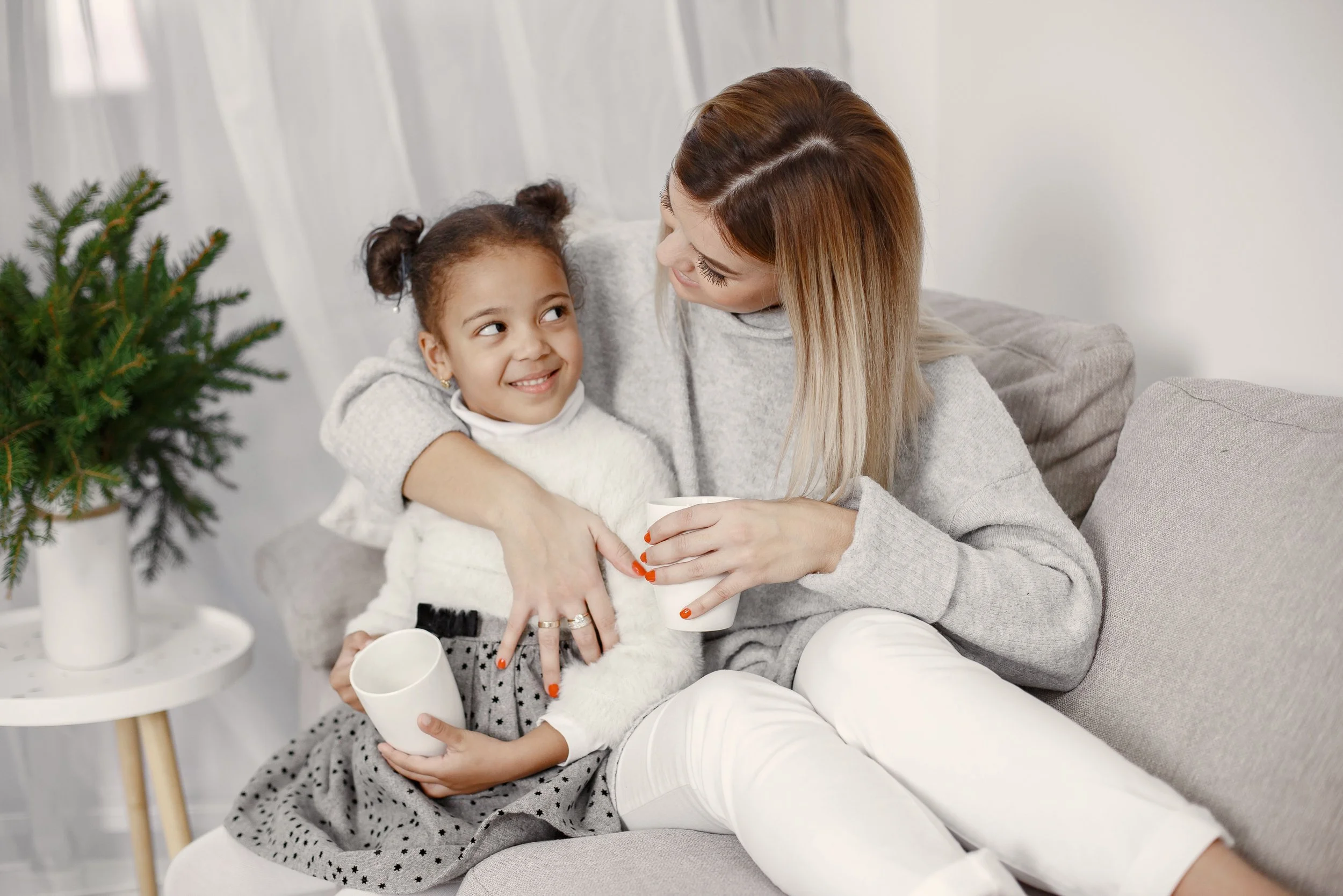 Mom smiling at her daughter while sitting together on a couch at home.