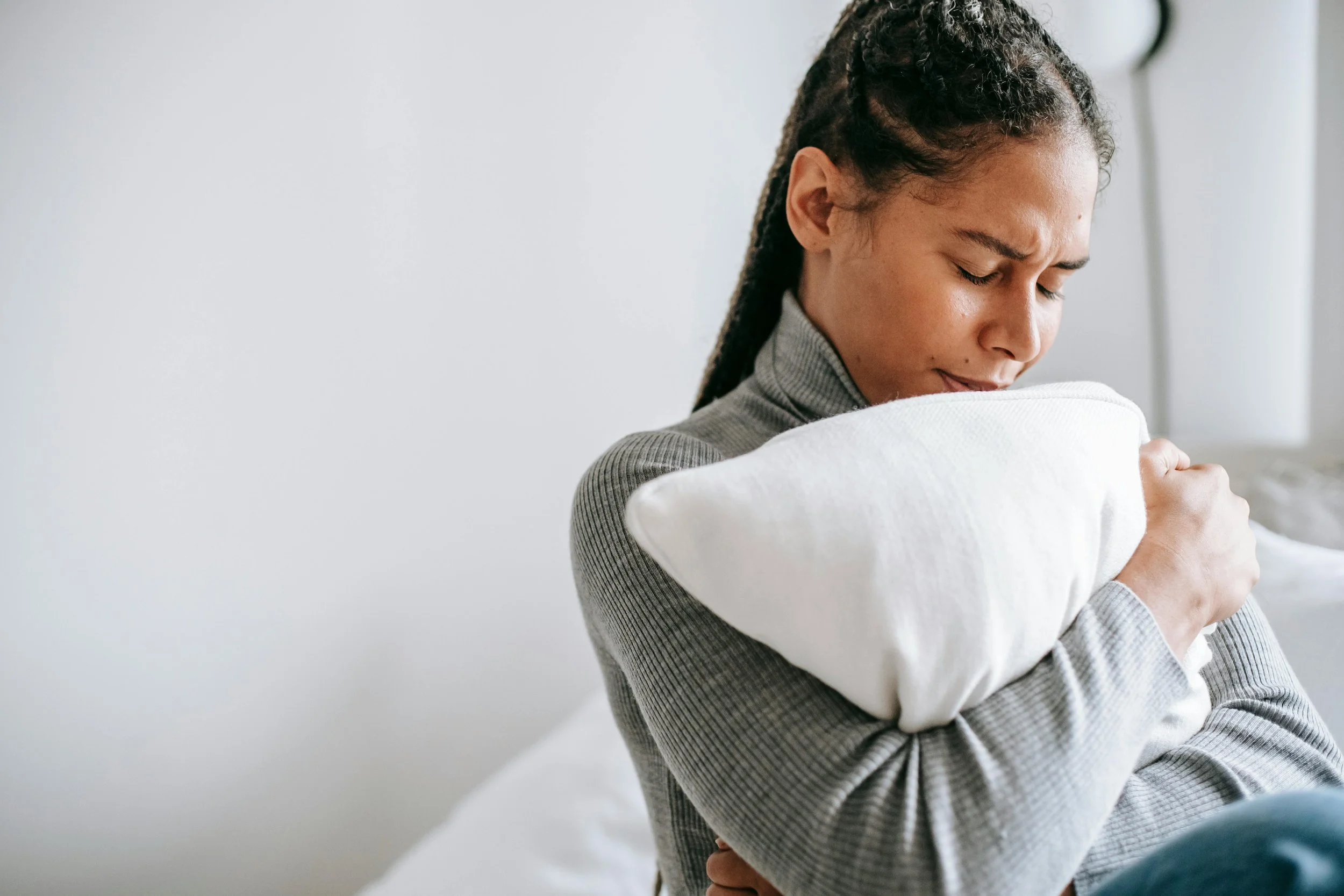 Woman practicing somatic therapy during a counseling session, eyes closed while gently hugging a pillow to promote grounding and nervous system regulation.