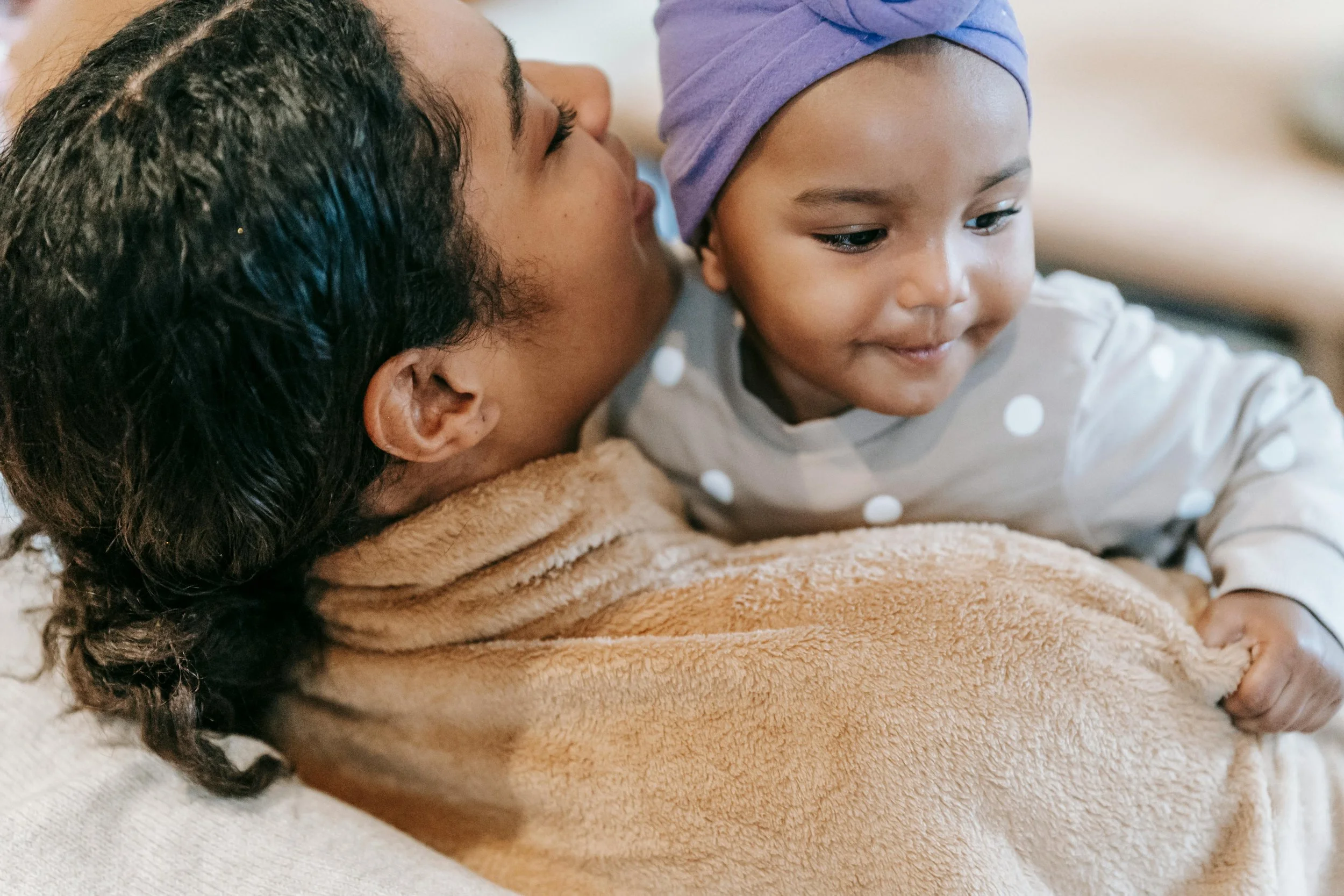 Mother holding her baby while sitting in bed, capturing a calm postpartum bonding moment in a cozy bedroom setting.