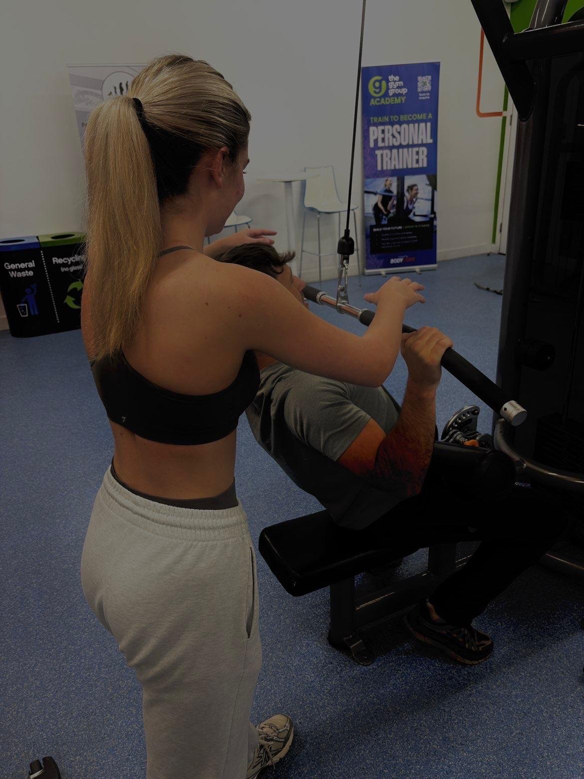 A woman encouraging a man to exercise on a weight machine at a gym.