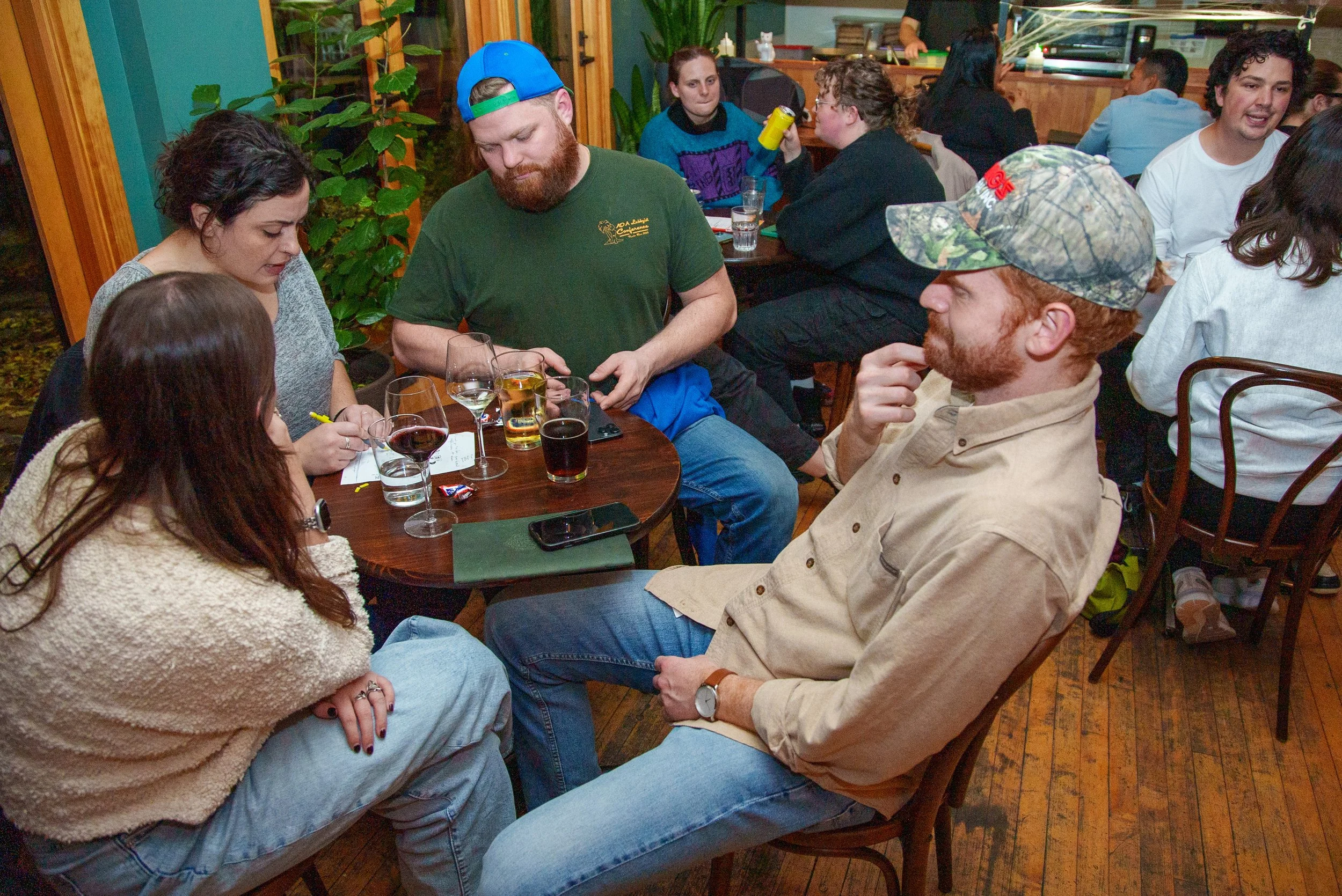 A group of people playing trivia gathered around a table at a restaurant, engaged in conversation and drinking beverages.