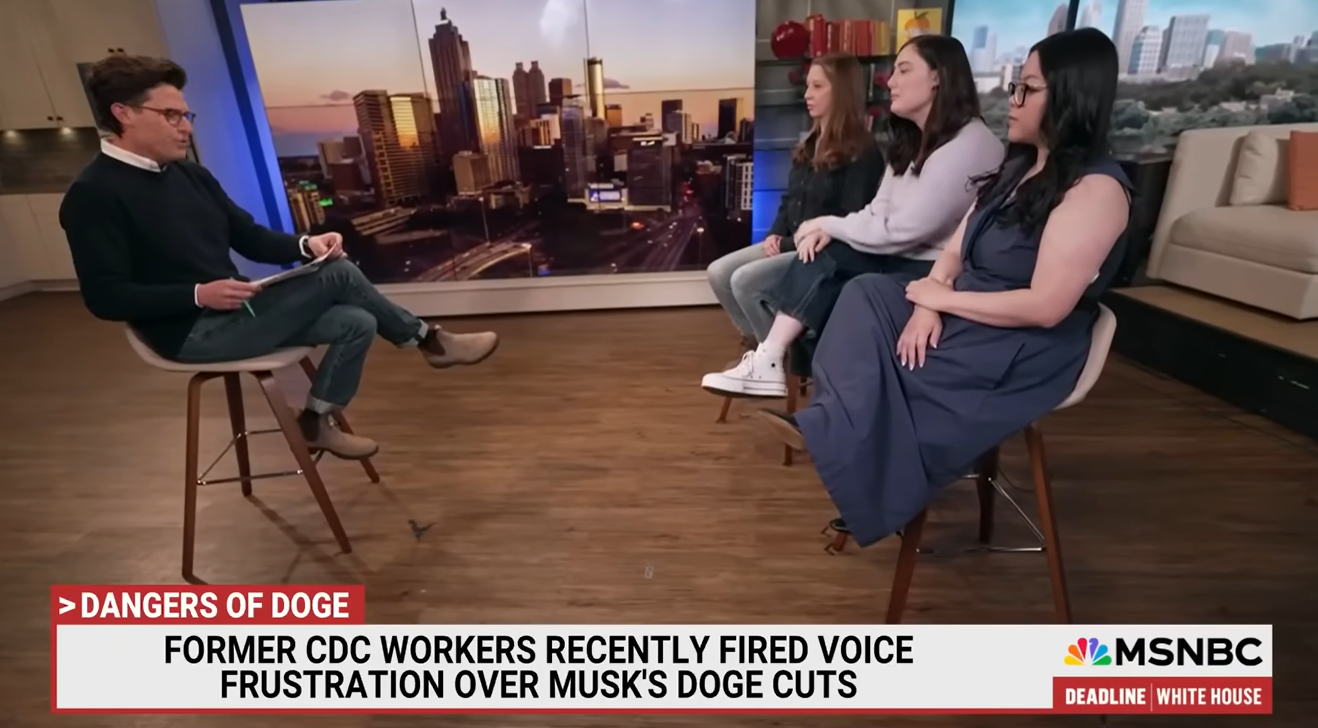 A man is sitting on a chair, holding papers, facing three women seated on chairs. The background shows a city skyline at sunset on a screen. The scene appears to be a television interview on MSNBC discussing dangers of doge, with a news ticker mentioning former CDC workers and Elon Musk.