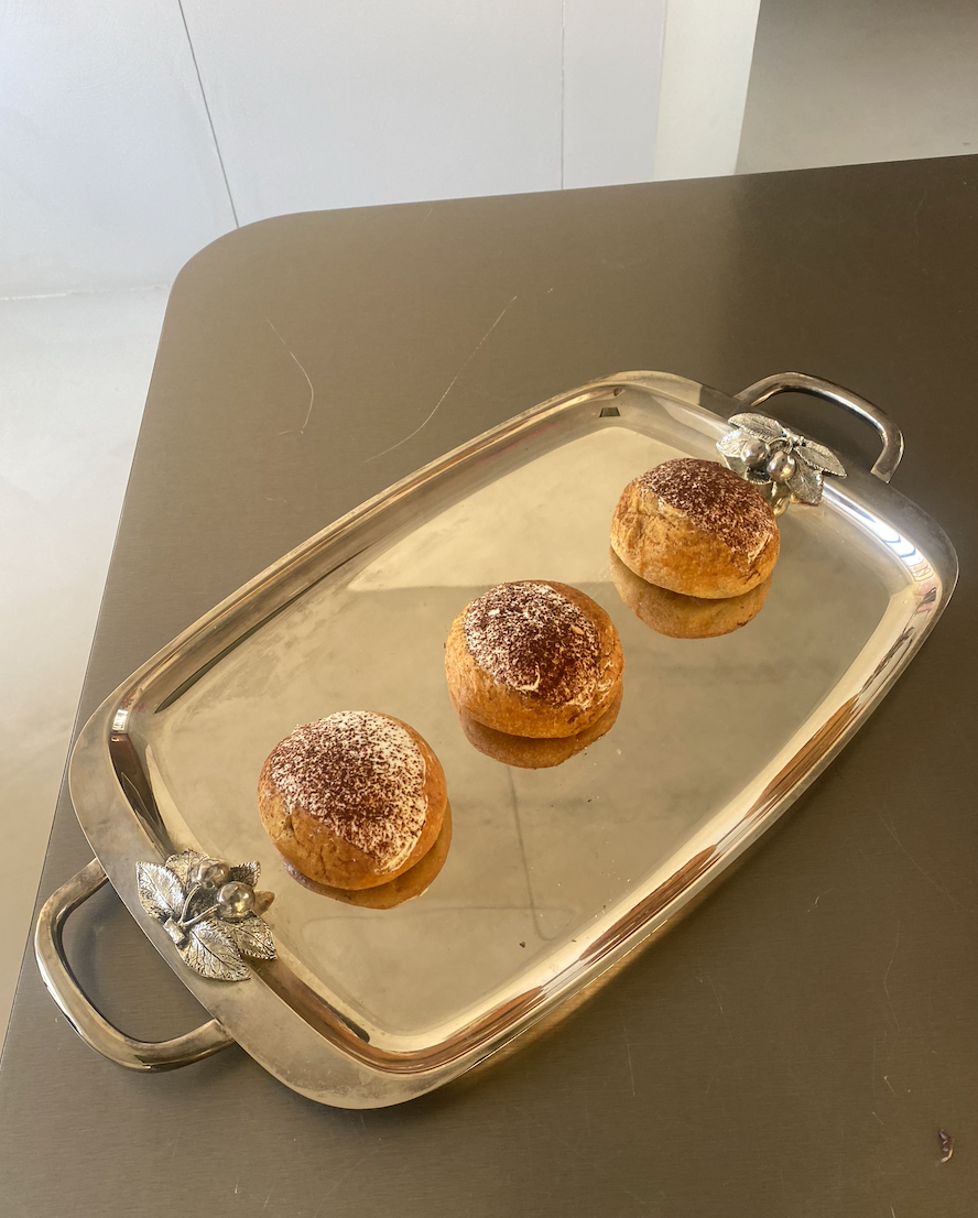 Trois petits pains recouverts de sucre, placés sur un plateau en métal argenté avec des décors de feuilles et de baie, posé sur une table.