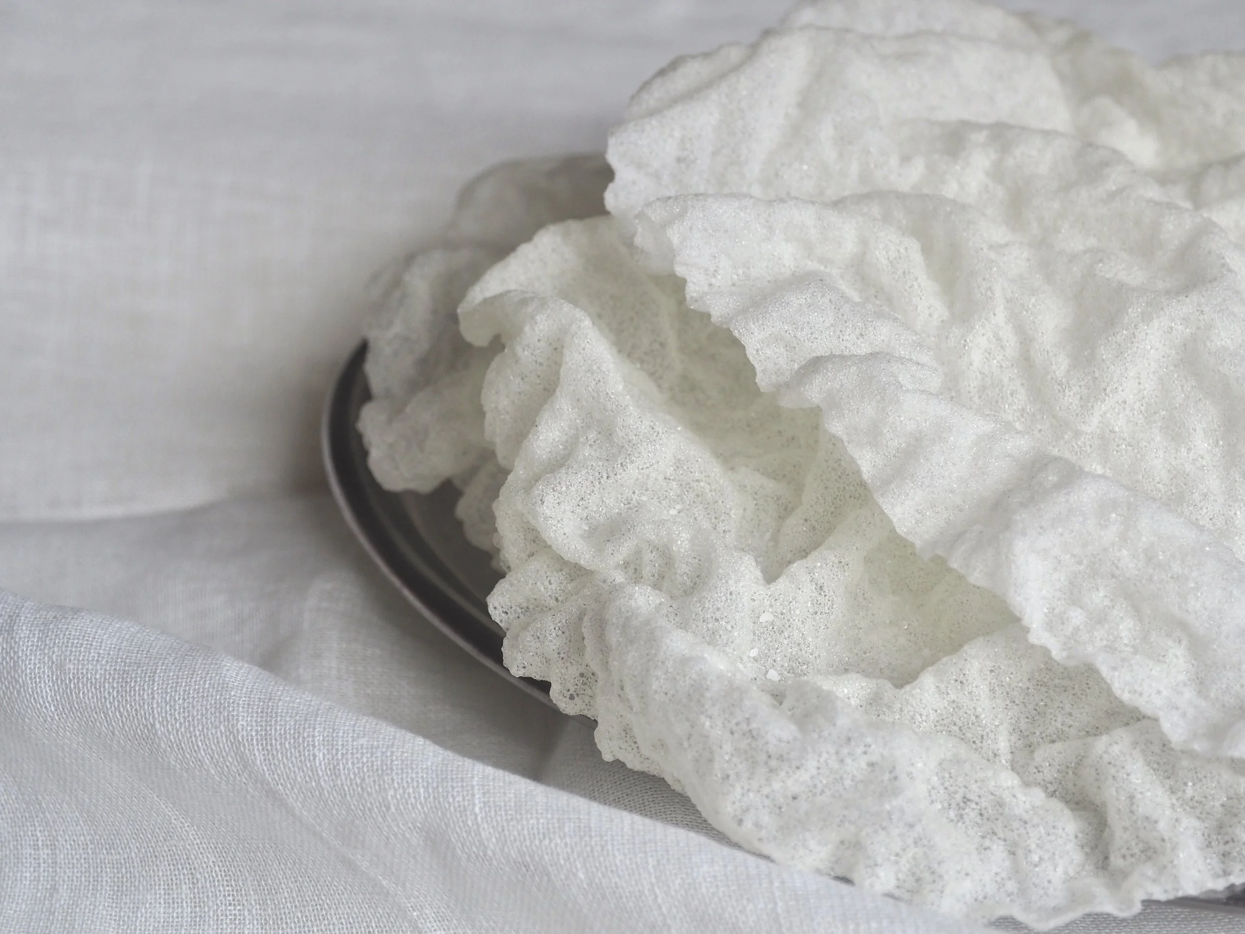 Meringue blanche sur une assiette en céramique, posée sur un tissu blanc.