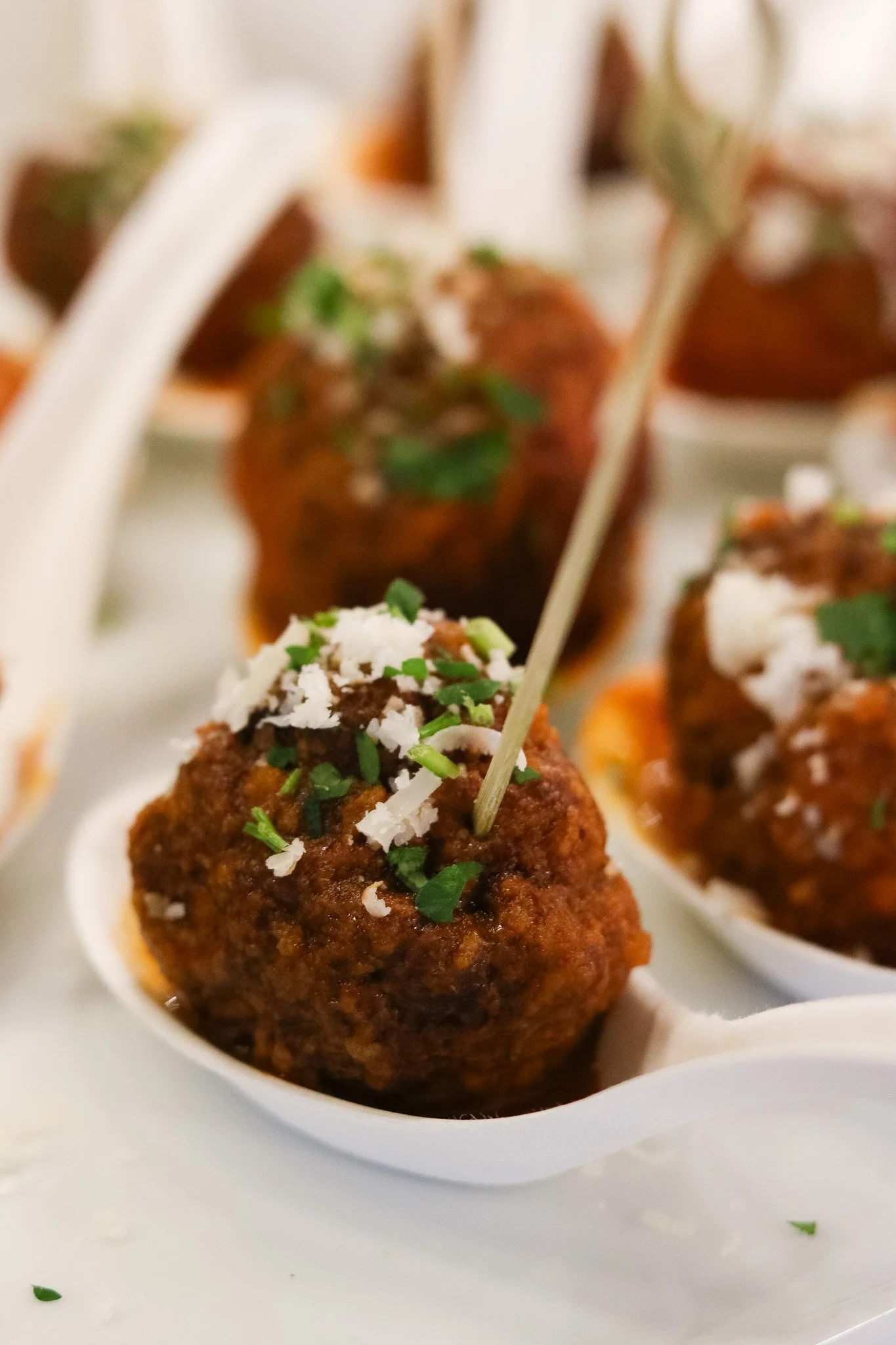 Close-up of a serving of Italian-style meatballs topped with grated cheese and chopped herbs on a white dish.