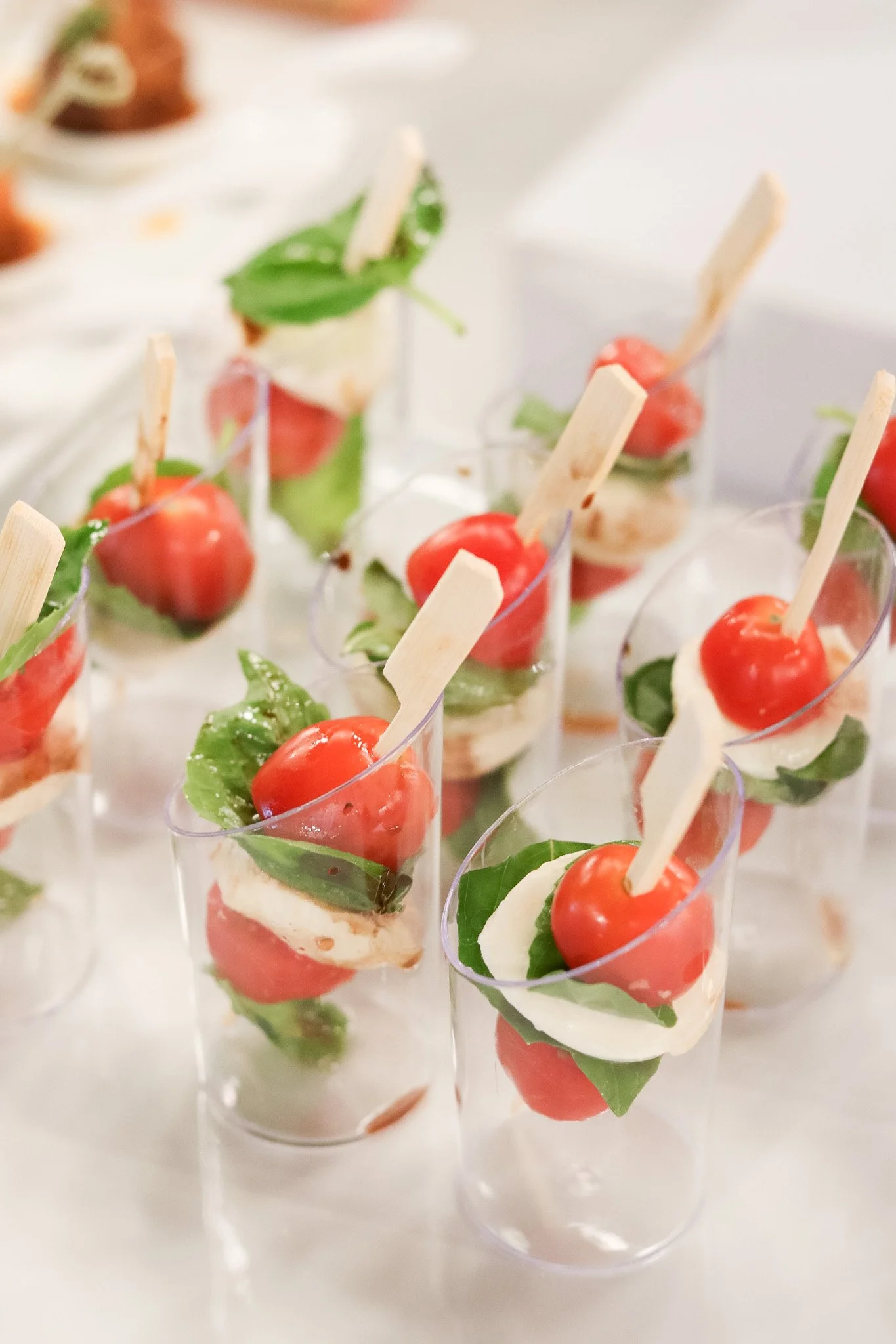 Individual serving cups with cherry tomatoes, mozzarella cheese, basil leaves, and small wooden skewers.